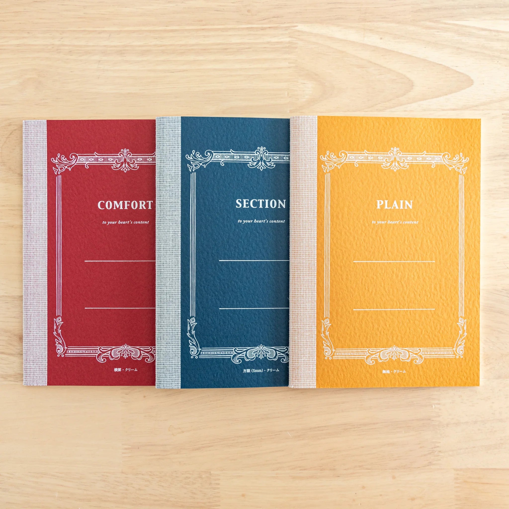 Three Japanese notebooks with decorative borders: red Comfort, blue Section, yellow Plain covers, cream-textured spines