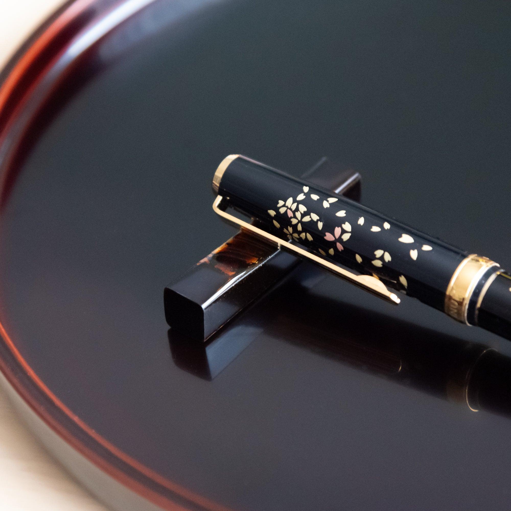 Hand-finished Echizen black lacquered sakura wood pen rest features gold speckle detail accent, keeping pens secure during