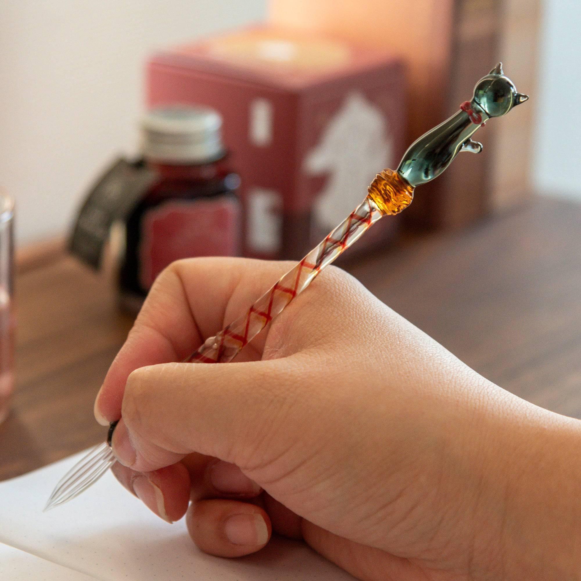 Black Nyanko cat glass dip pen in hand with dark green cat figurine and red-orange striped handle bands