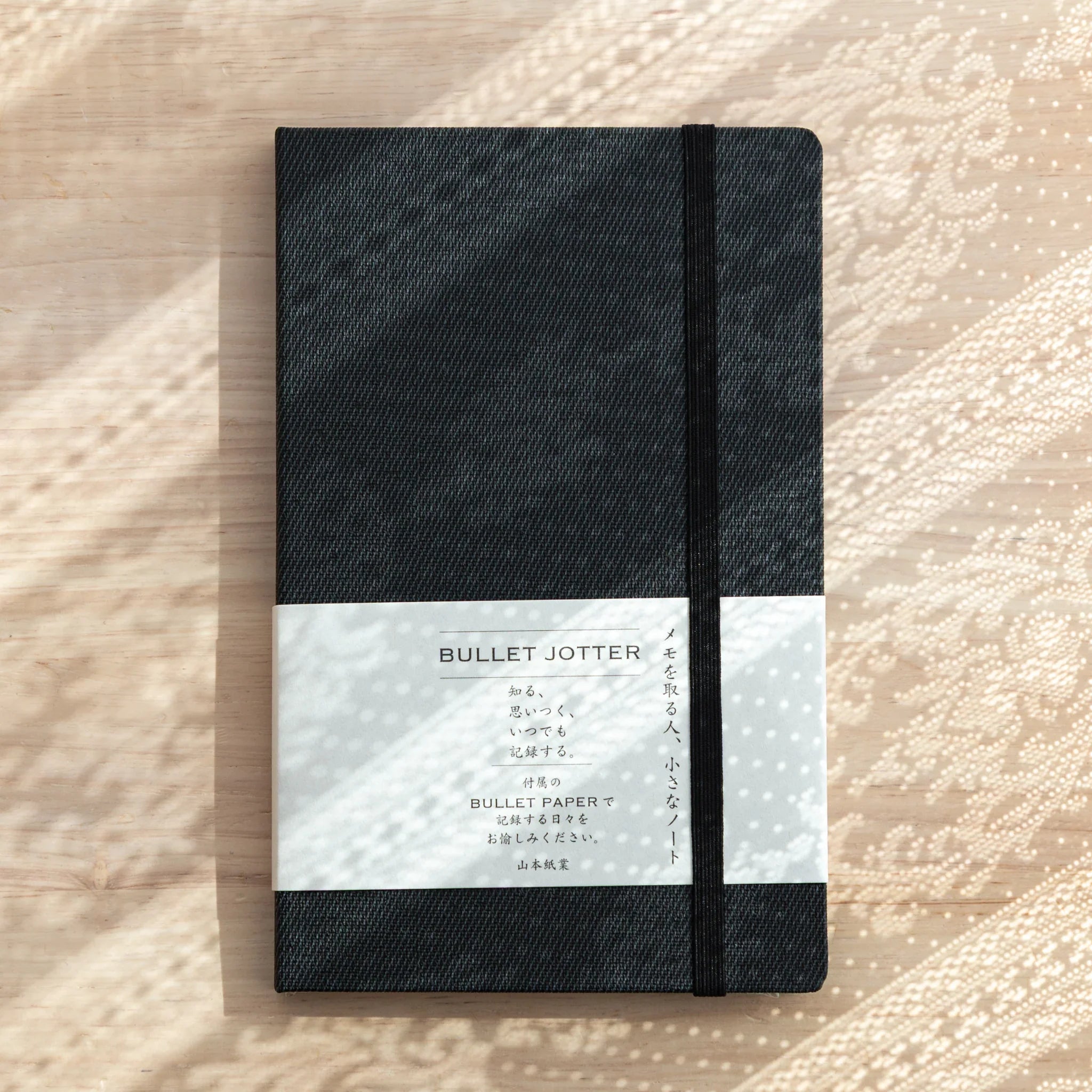 Bullet Jotter black gabardine cover closed, white belly band with BULLET JOTTER title, black elastic band, textured surface