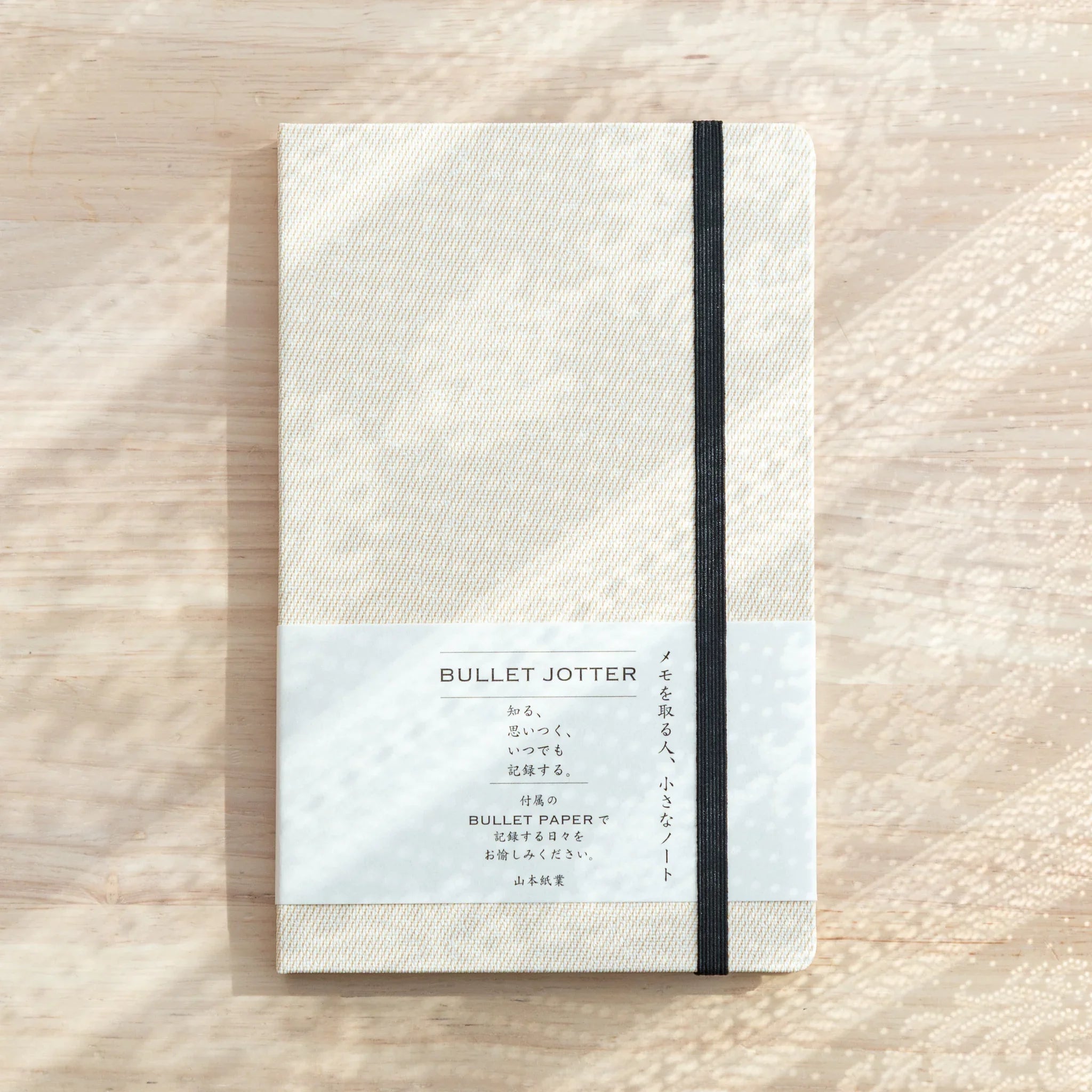 Bullet Jotter ivory white gabardine cover closed on light wood, black elastic band, belly band with BULLET JOTTER text