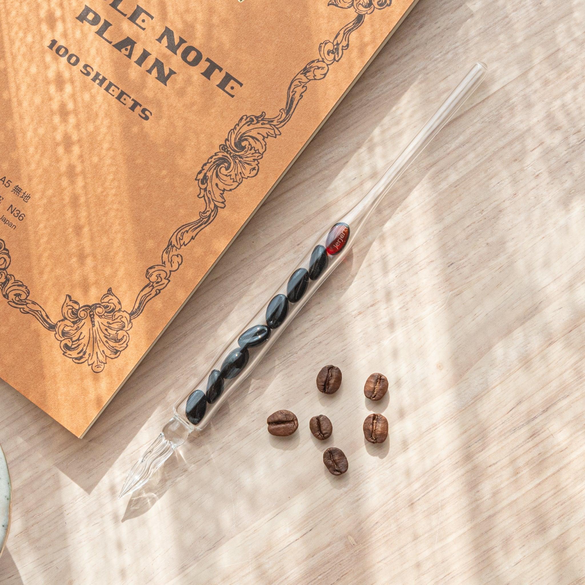 Glass dip pen with dark roasted coffee beans suspended inside clear barrel, red bead accent at top portion shown