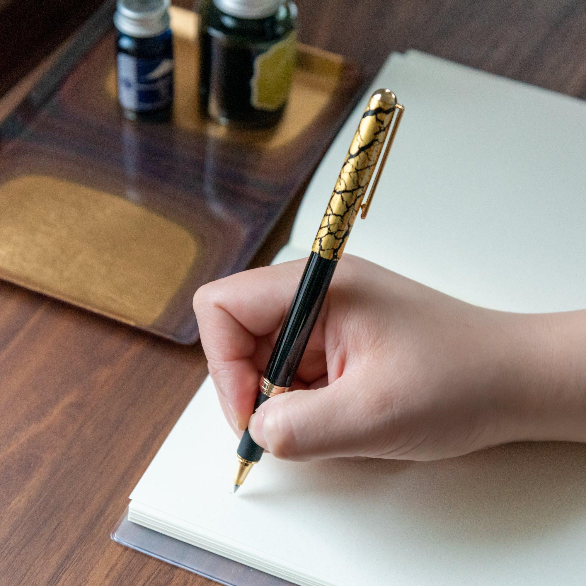 Japanese crack pattern gold leaf black ballpoint pen with gold crackle cap displayed beside uncapped barrel