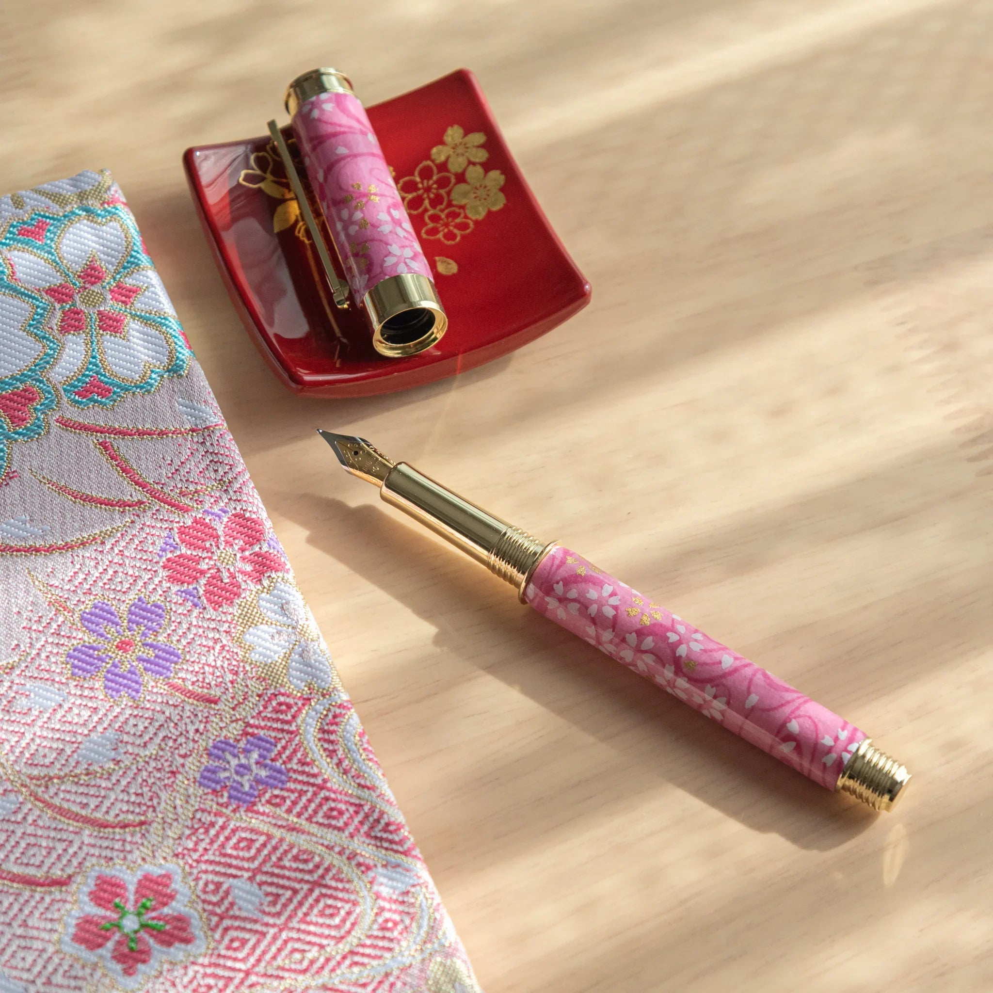 Pink Mino washi Japanese fountain pen uncapped showing gold nib, with cap resting on a red lacquer tray on a wooden surface