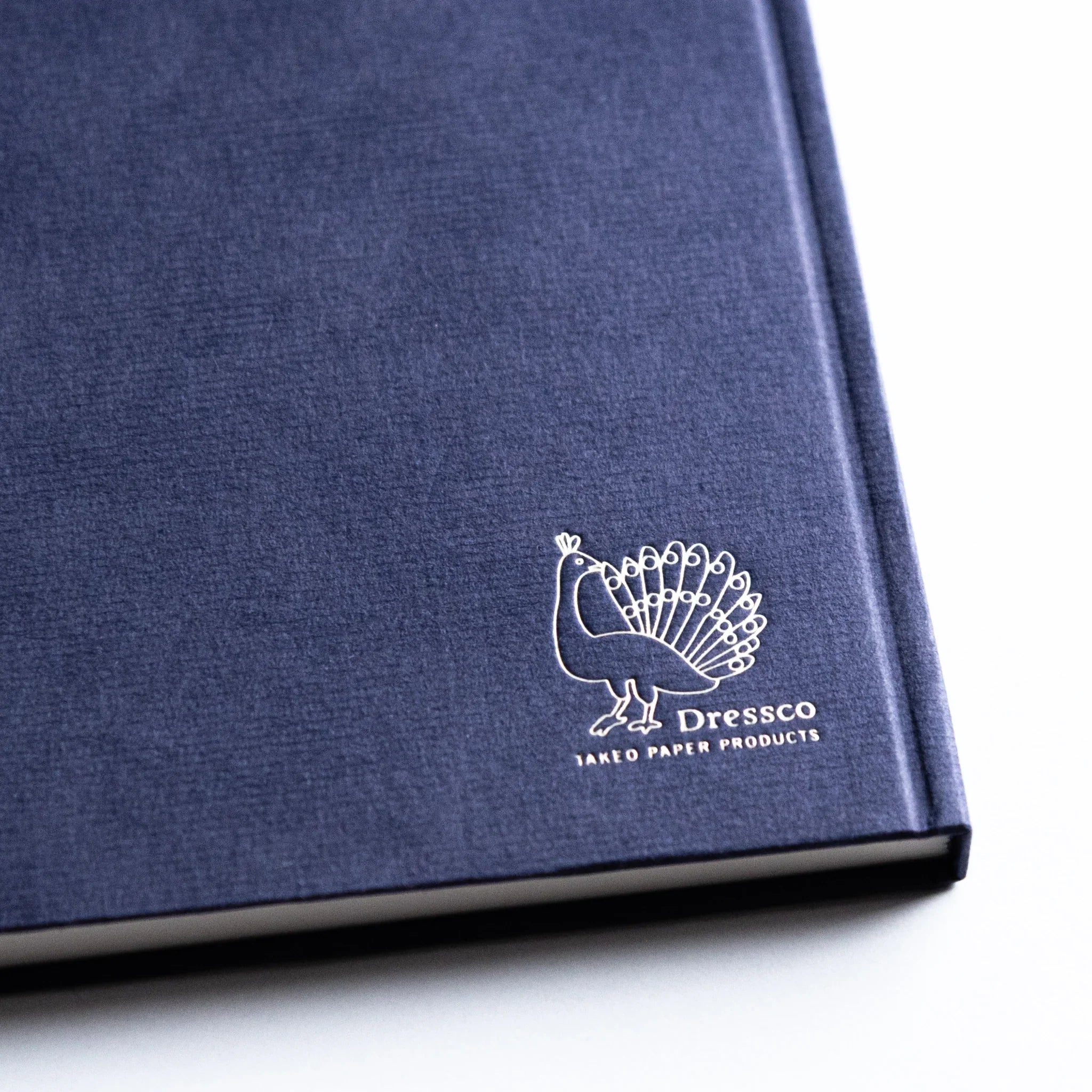 Dressco Bank Ledger Paper A6 notebook lying flat showing the cover face and stitched edge from a top-side angle
