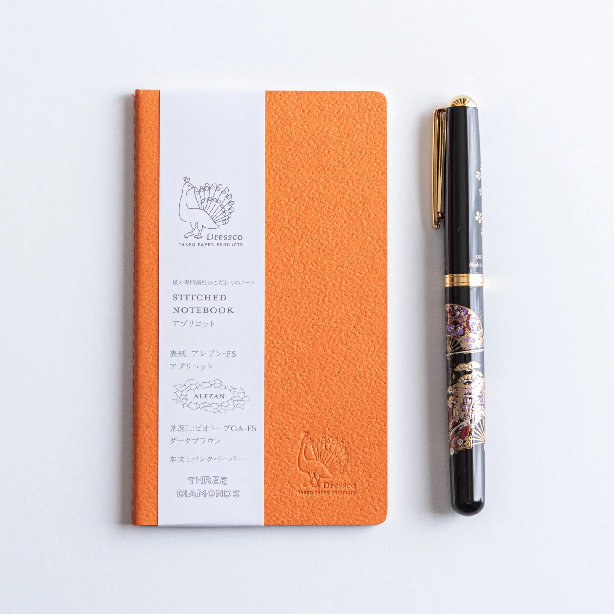 Orange textured fabric cover of A6 Dressco Bank Ledger Paper stitched notebook displayed on white background surface