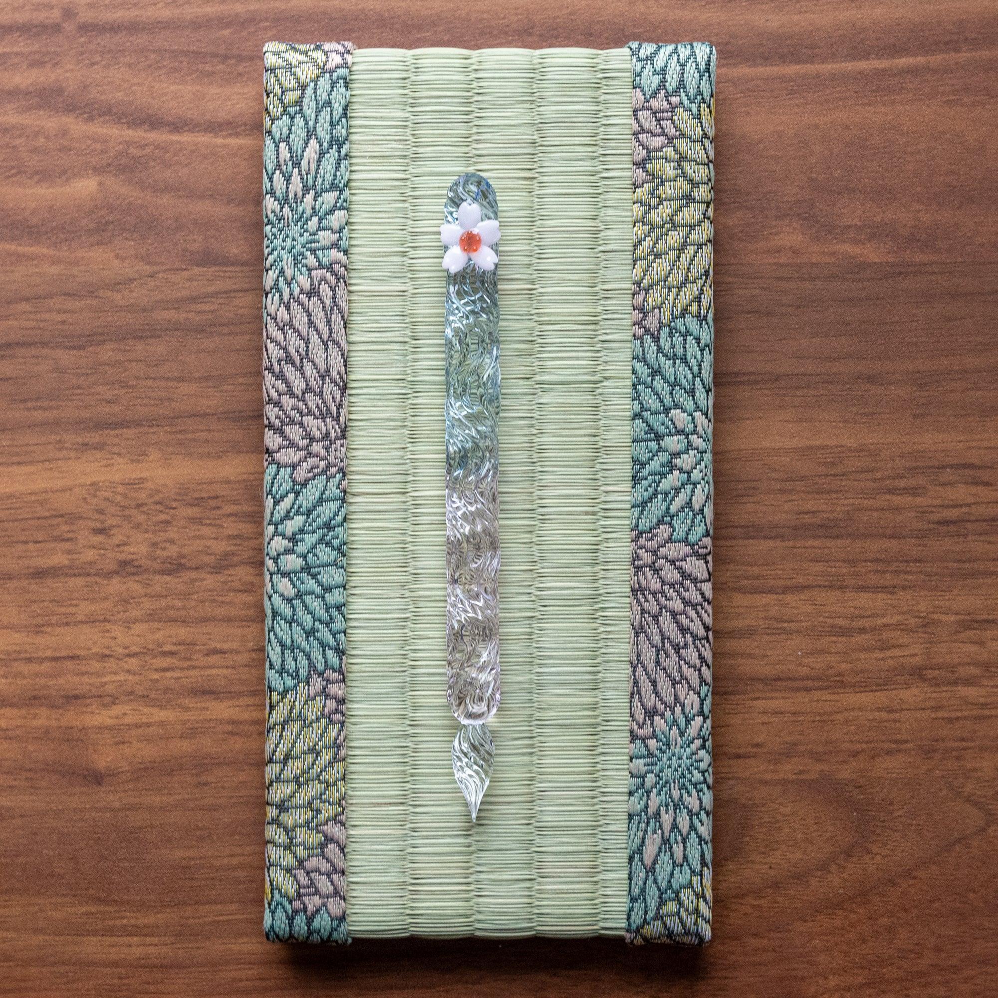 Glass pen with white ceramic flower tip resting in Chrysanthemum Tatami Pen Tray on walnut wood desk