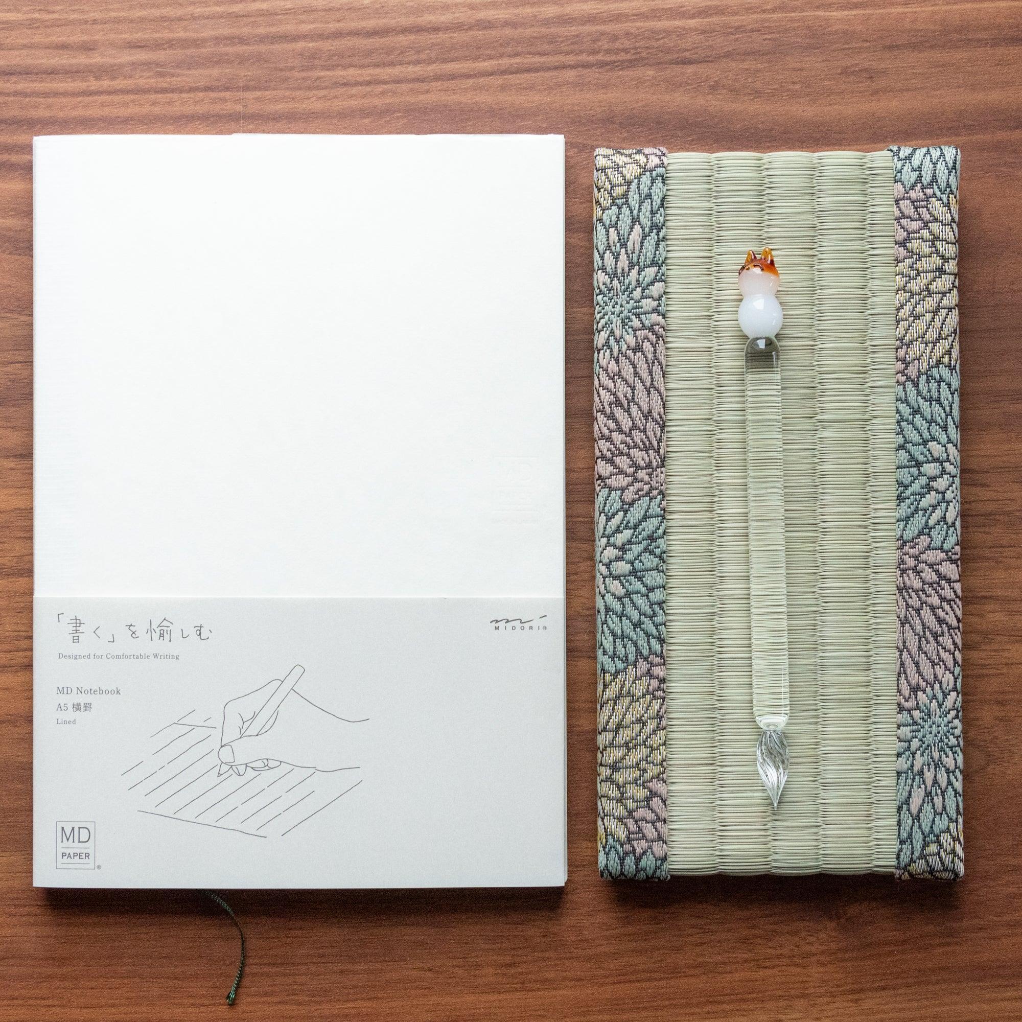 Chrysanthemum Tatami Pen Tray with glass dip pen topped with white bird figurine beside MD Notebook A5 on walnut wood