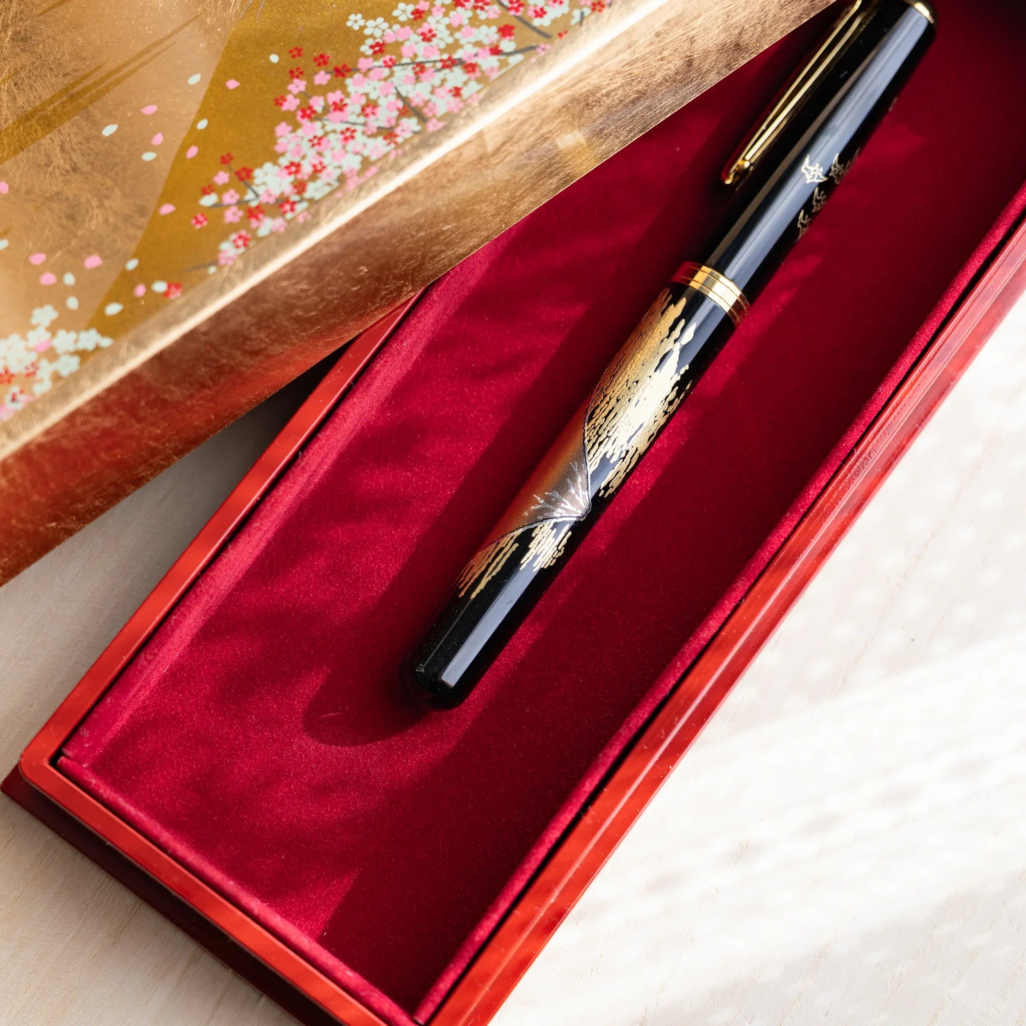 Yamanaka pen case positioned at angle showing gold exterior finish and decorative lid displayed clearly