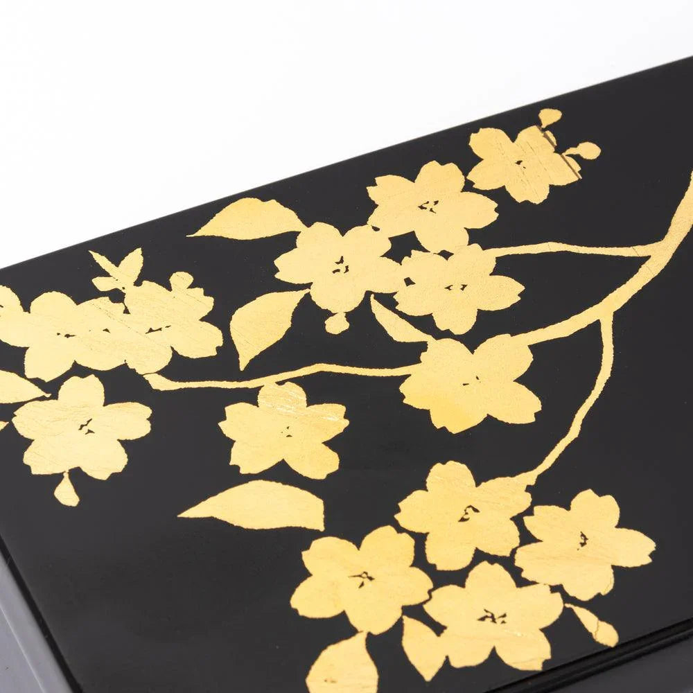 Corner view of black lacquer pen box lid with gold leaf sakura branch and flowers extending across the glossy surface