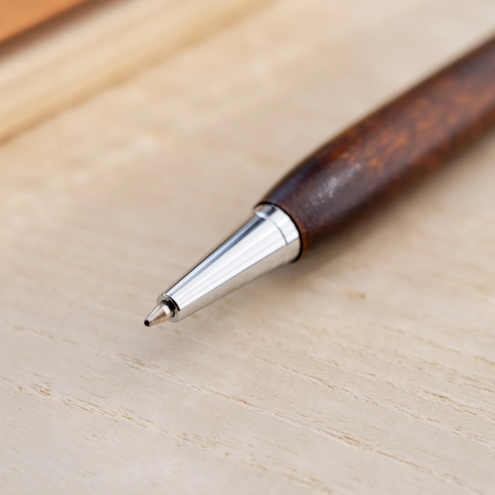 Amber-brown horse chestnut wood urushi ballpoint pen, close-up of silver cone tip and writing point, Japanese wood