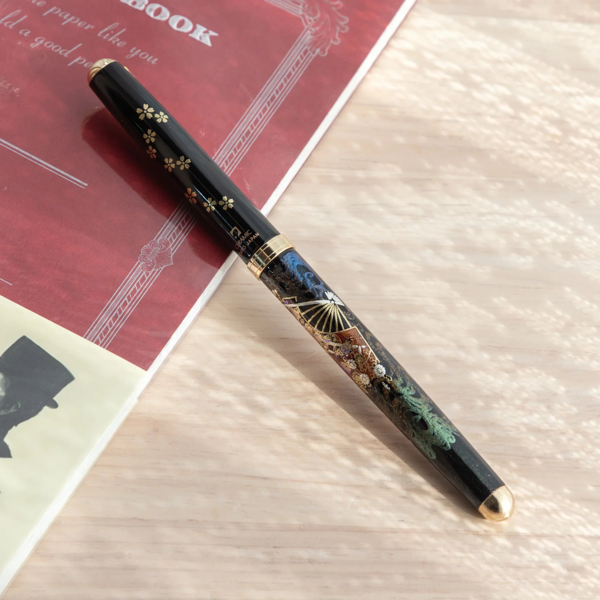Black Yamanaka Japanese ballpoint pen rotated showing blue and teal maki-e lacquer barrel motifs with gold sakura cap