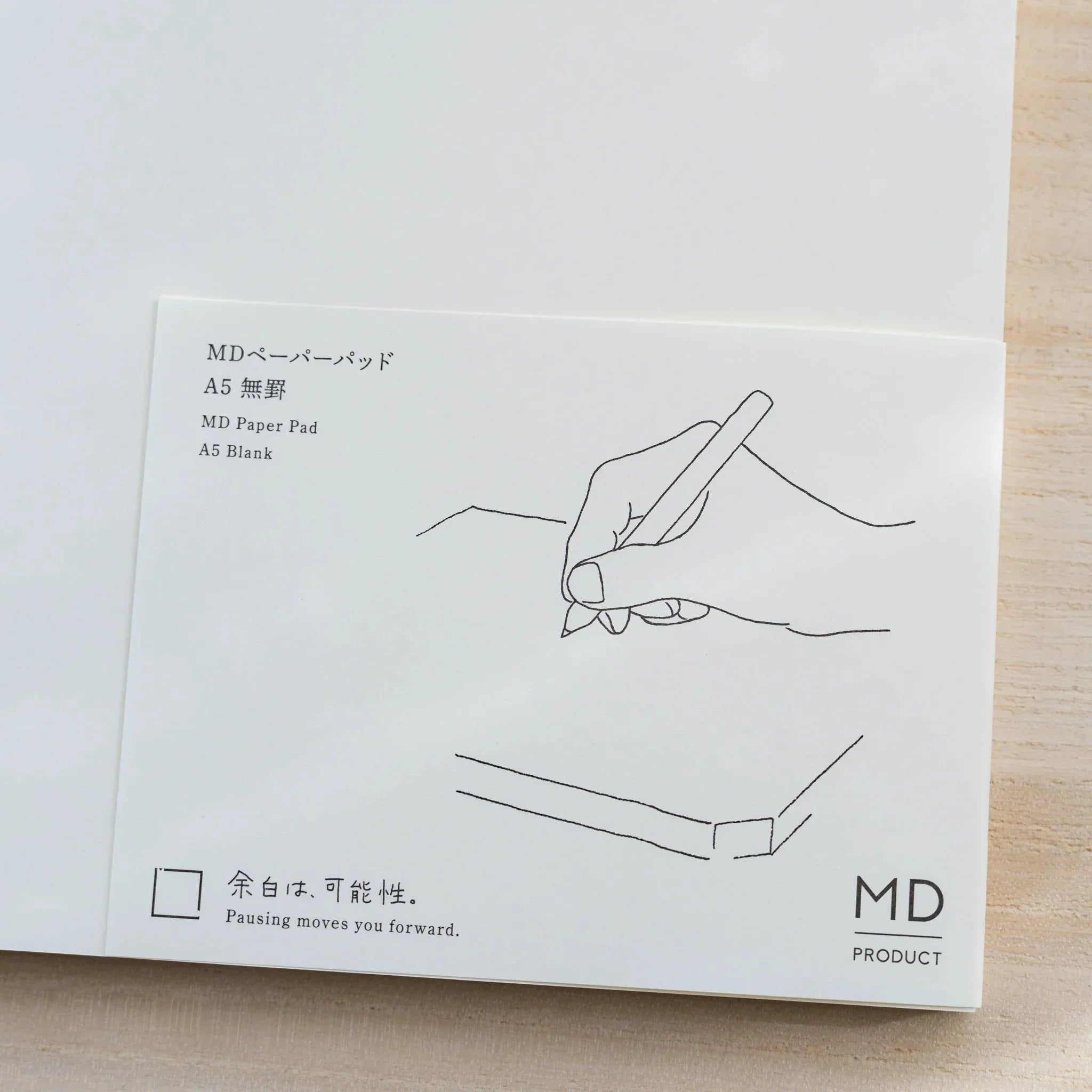 Close-up of Midori MD Paper Pad A5 paper belly band, line drawing of a hand writing and text MD Paper Pad A5 Blank