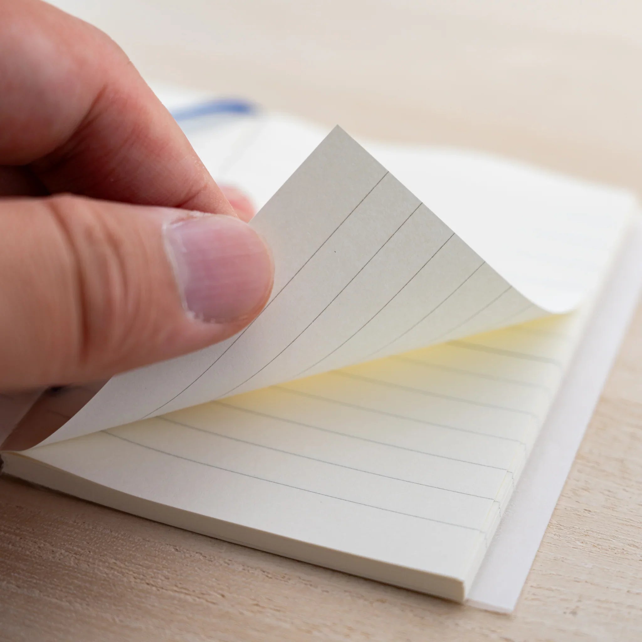Hand fanning the cream pages of an MD Notebook A7 showing the page block