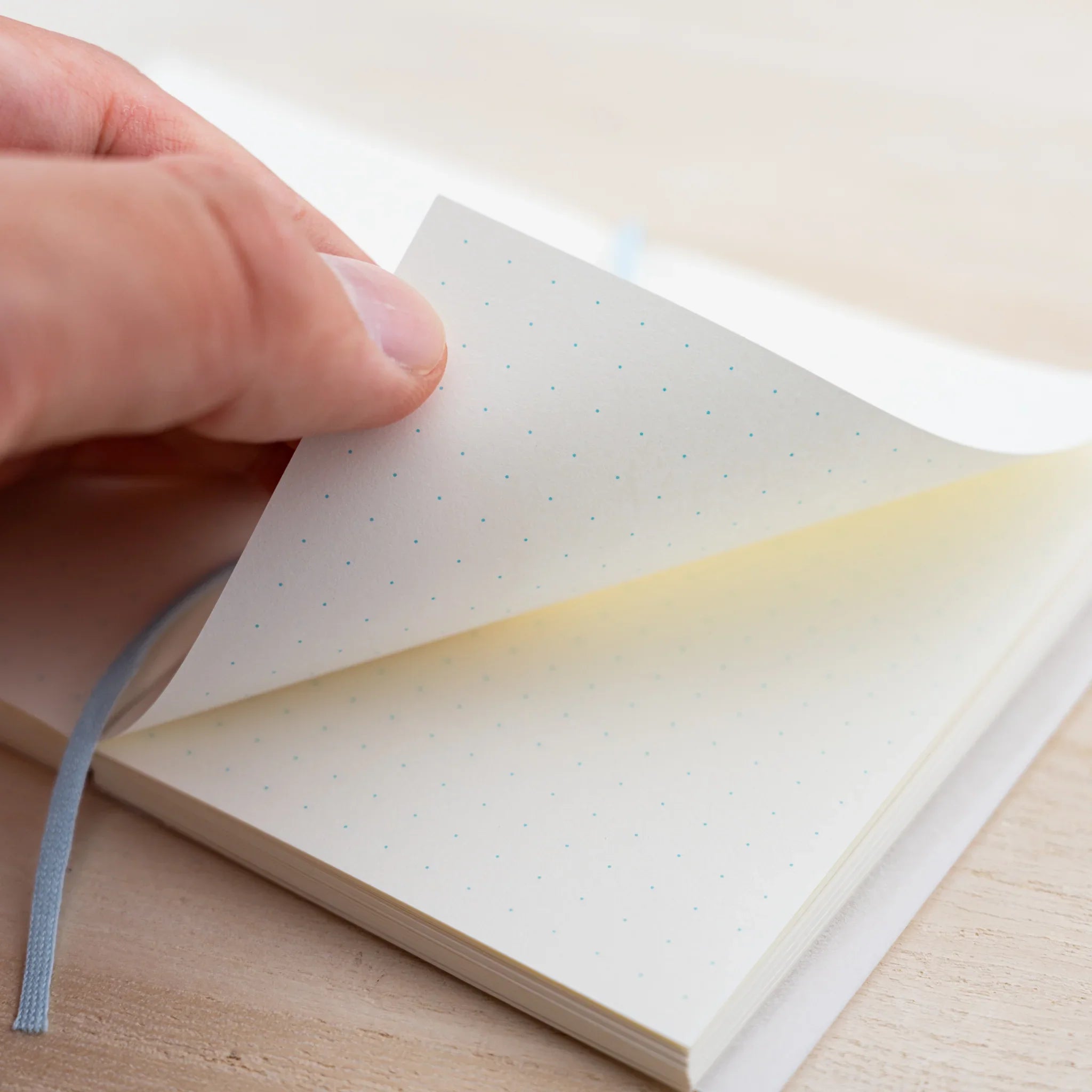 Hand turning a dot grid page of an MD Notebook A7 showing the cream page block