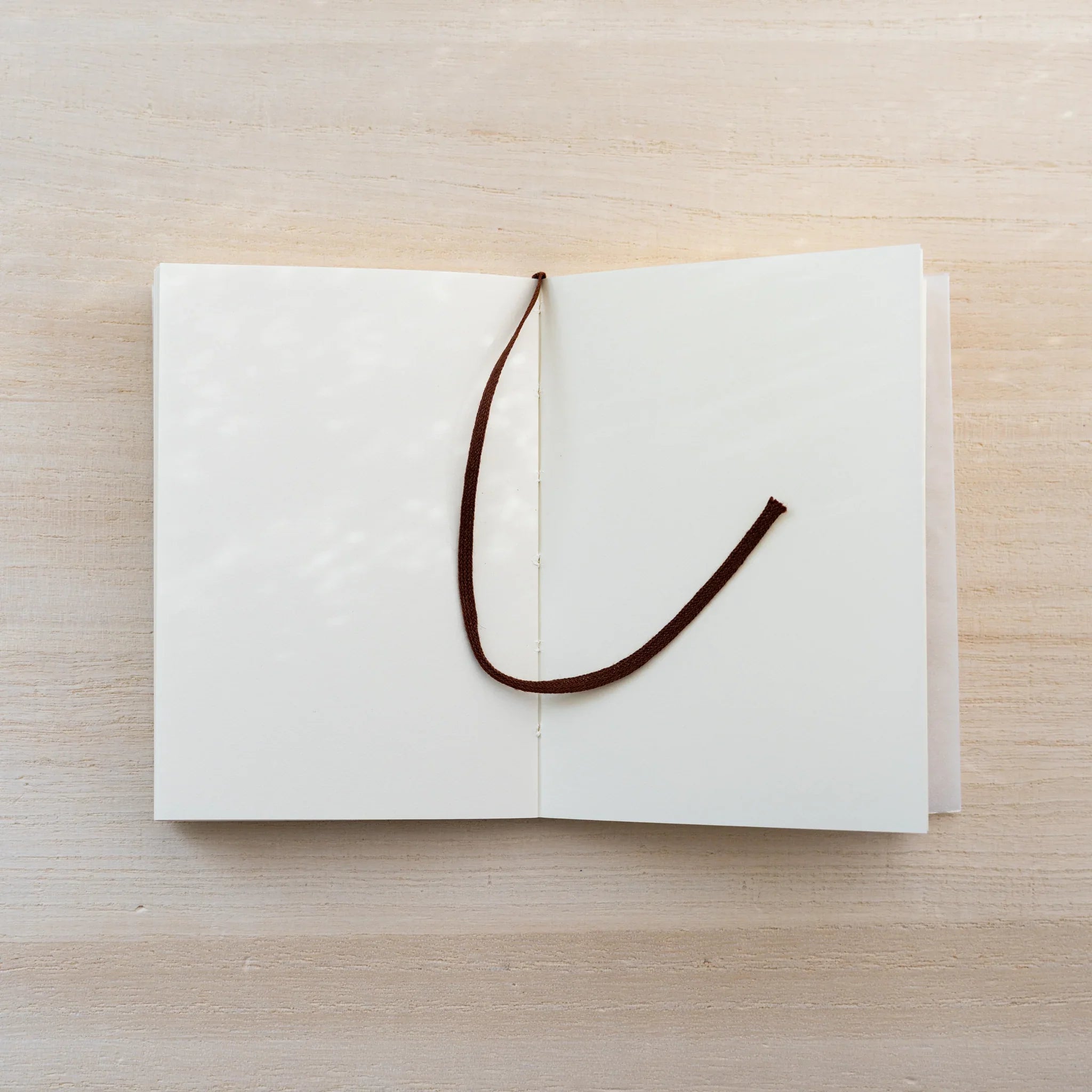 MD Notebook A7 opened flat with a brown bookmark ribbon across a cream spread