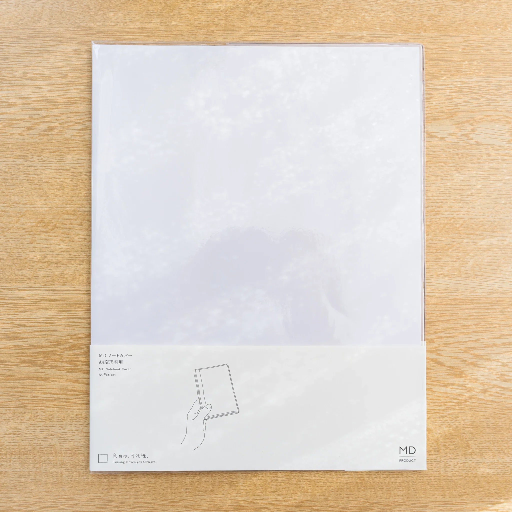 Clear PVC Midori MD Notebook Cover fitted over a white MD notebook with paper belly band, closed front view on wood