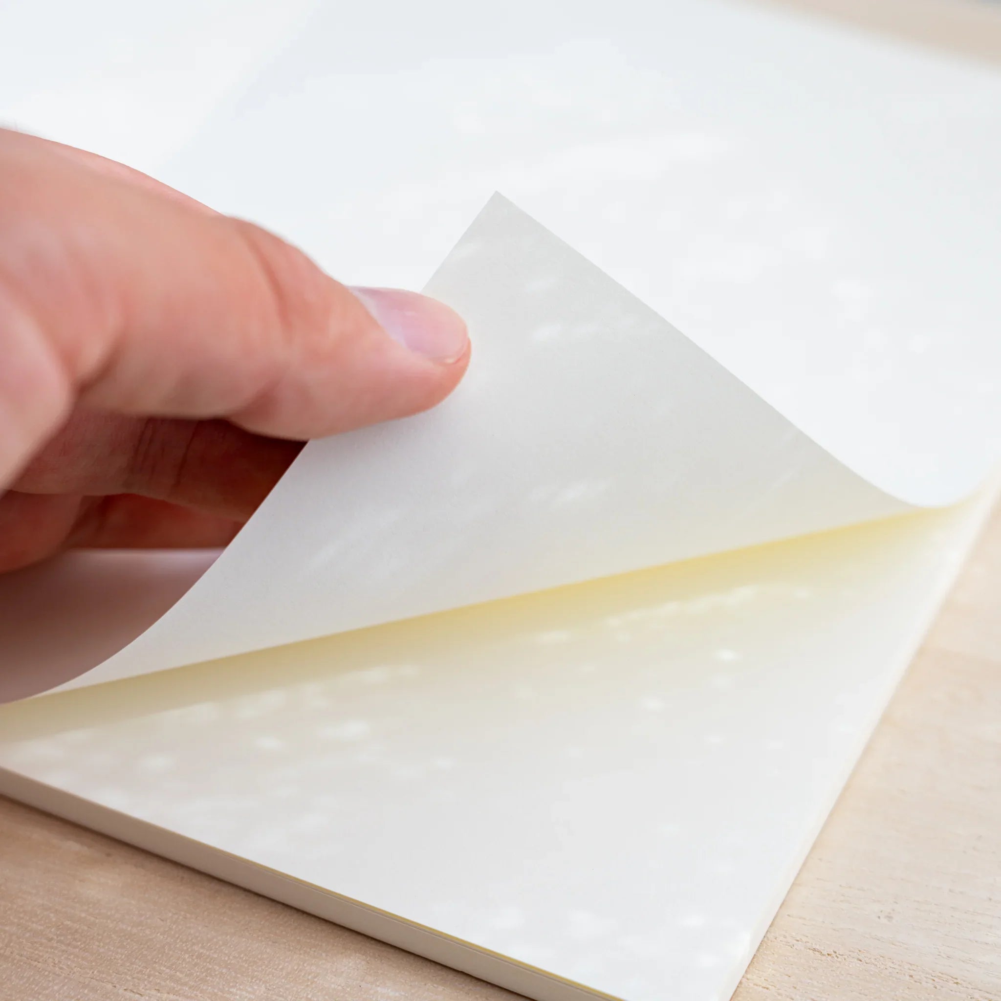 A hand lifting a blank cream page of an open Midori MD Notebook Thick, showing the thick paper