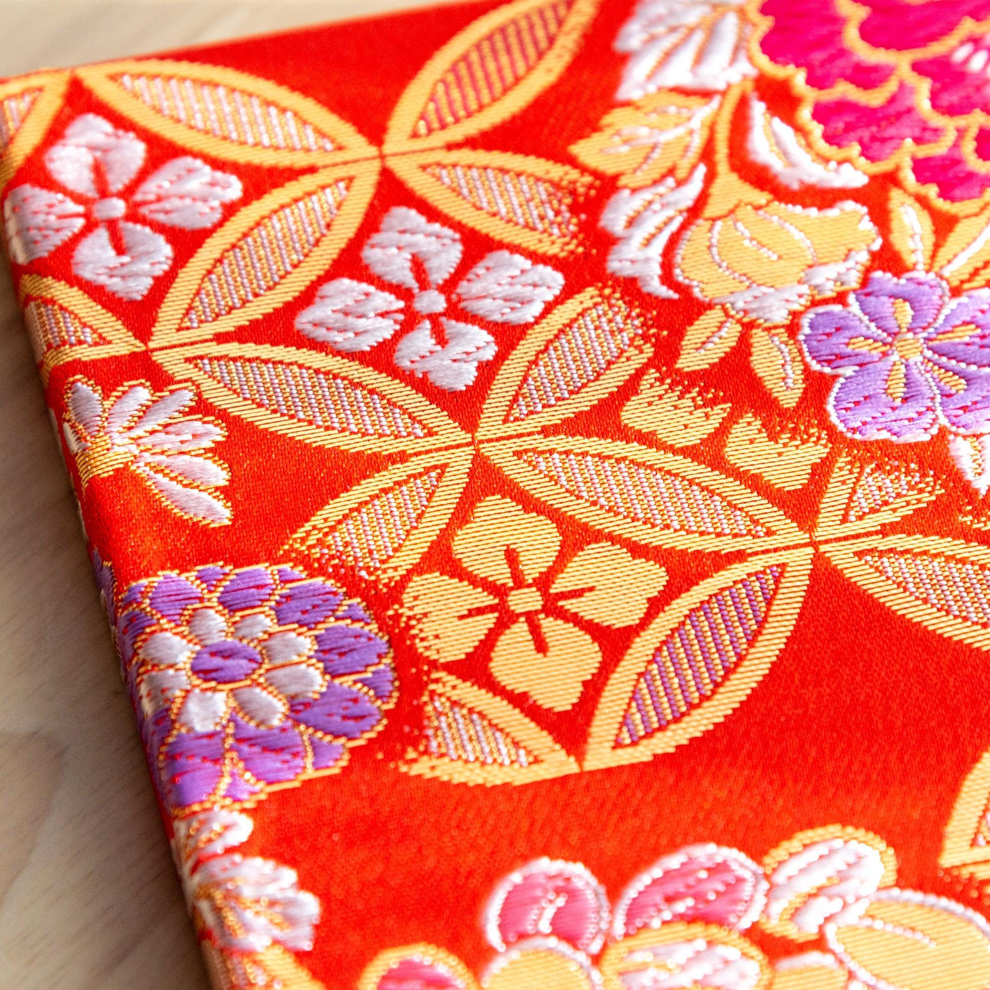 Corner close-up of Nishijin woven textile notebook in orange-red with gold shippo lattice and woven sakura and peony motifs