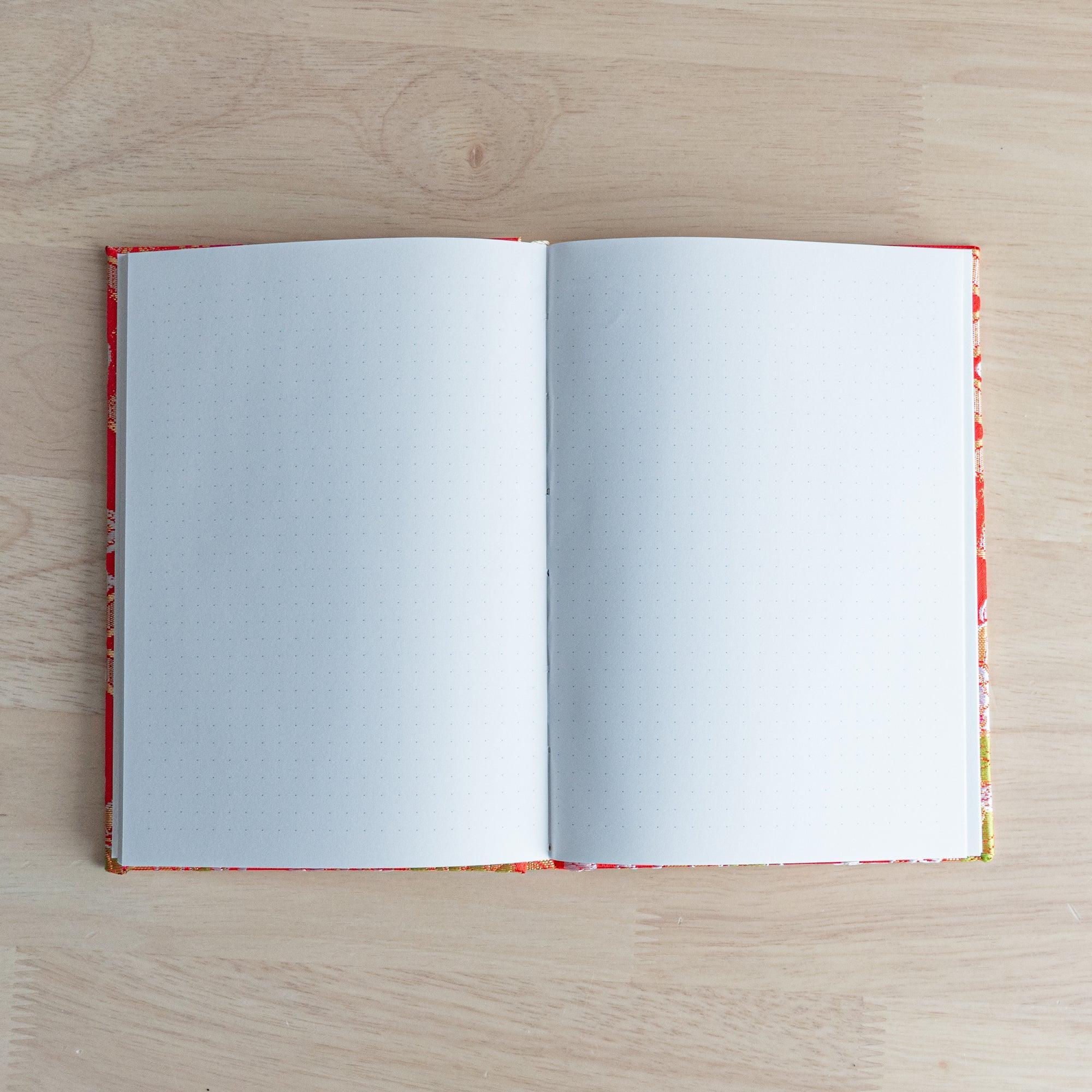 Opened Nishijin textile Japanese notebook showing two blank dot grid pages with woven textile cover visible on both edges