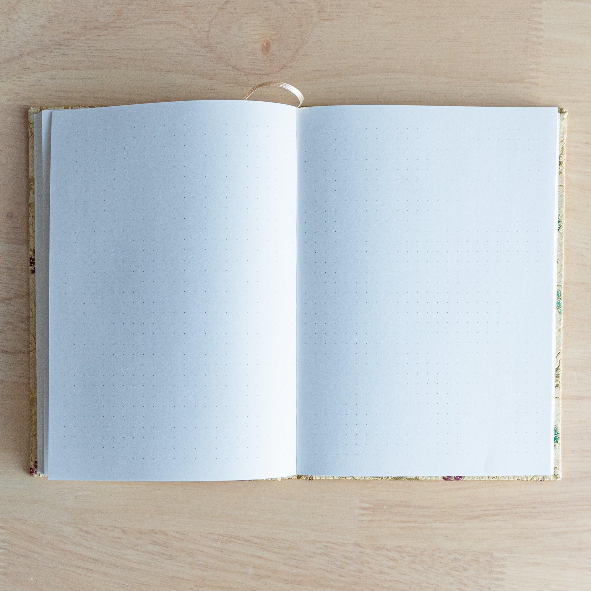 Opened Nishijin textile Japanese notebook showing two blank dot grid pages with gold textile cover and ribbon bookmark
