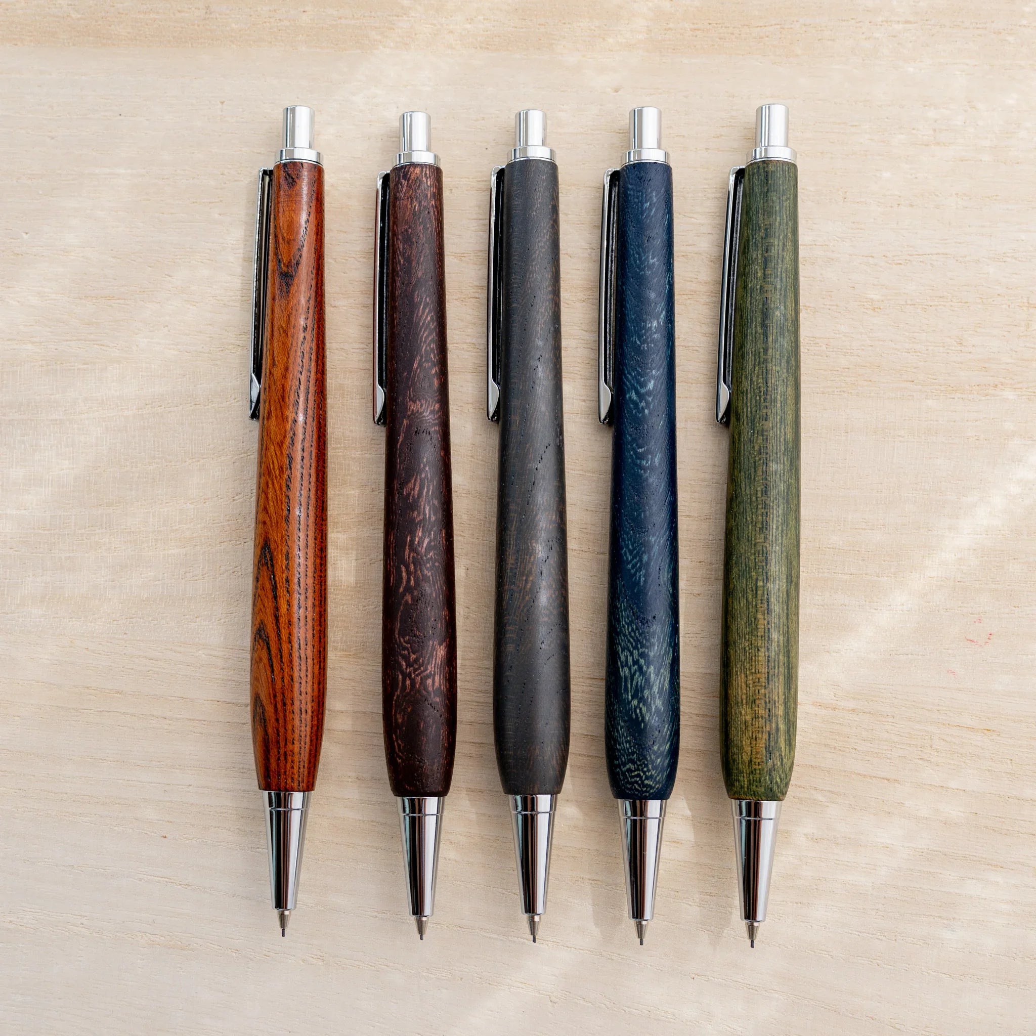 Five NIVI urushi lacquered mechanical pencils in amber, brown, charcoal, blue and green keyaki wood, side by side