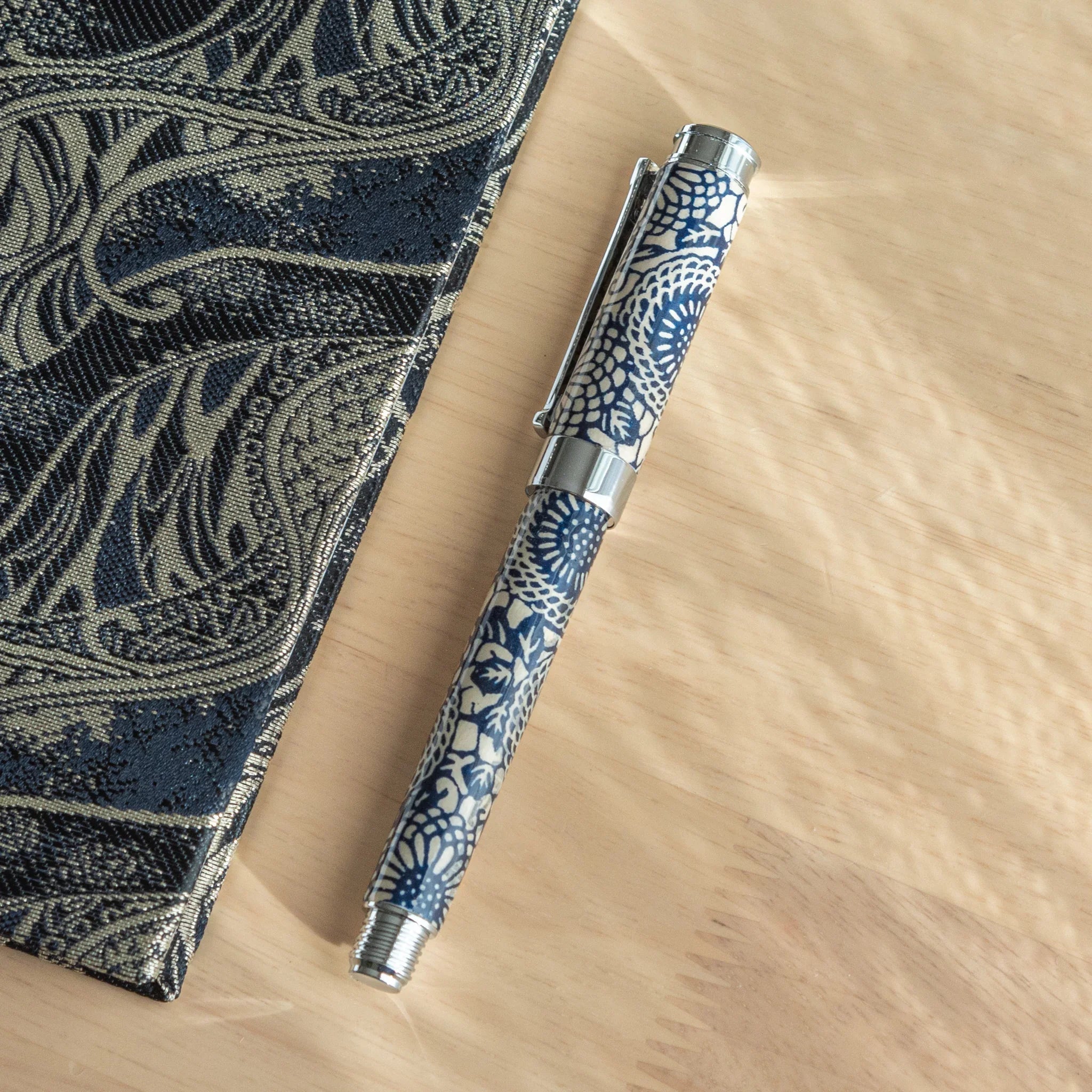 Peony Mino Washi fountain pen laid flat on blue botanical fabric showing navy wrapper with white peony flower cluster design