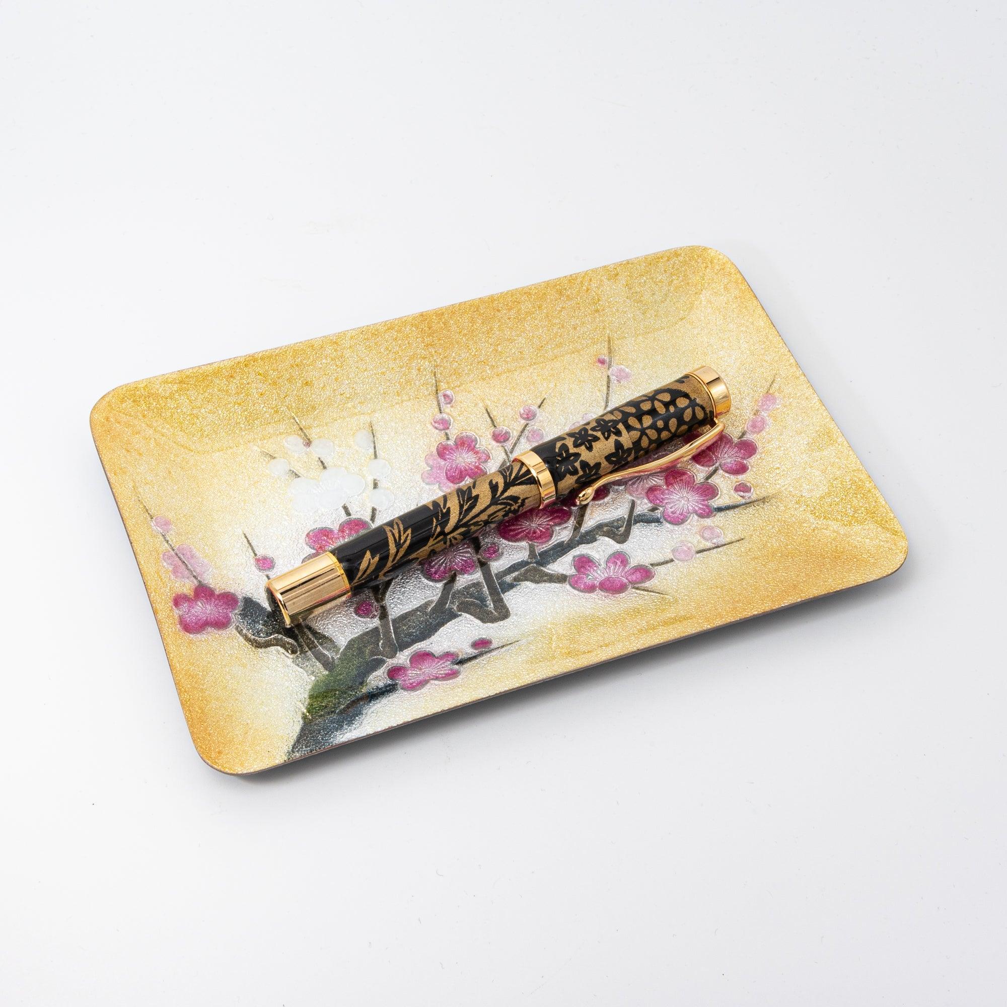 Plum shippo ware gold enamel pen tray on white background, angled view with black floral fountain pen resting inside