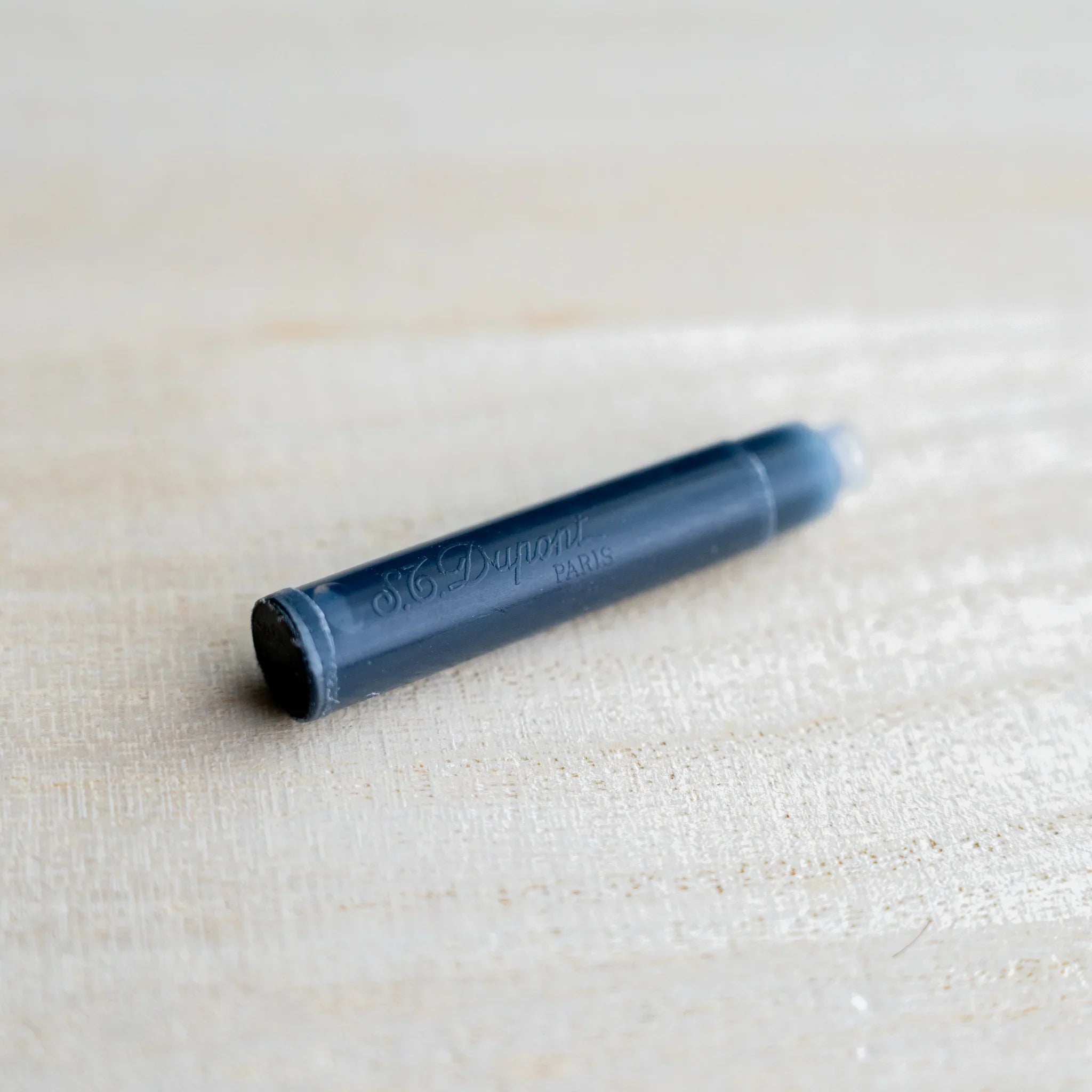 Single S.T. Dupont fountain pen ink cartridge in dark navy, embossed S.T. Dupont Paris, on light wood