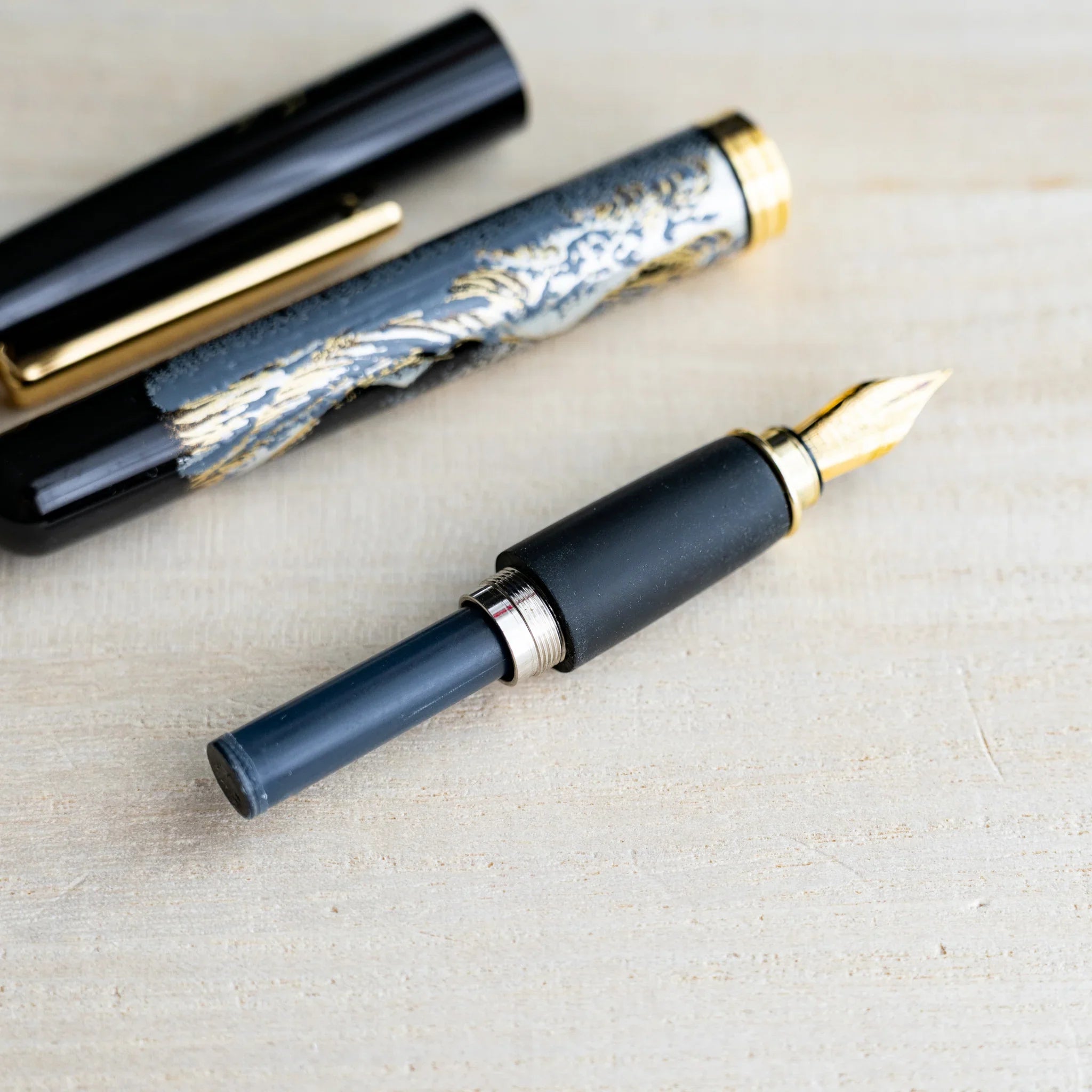Black Yamanaka pen grip section with gold nib and a navy S.T. Dupont ink cartridge attached, barrel and cap behind