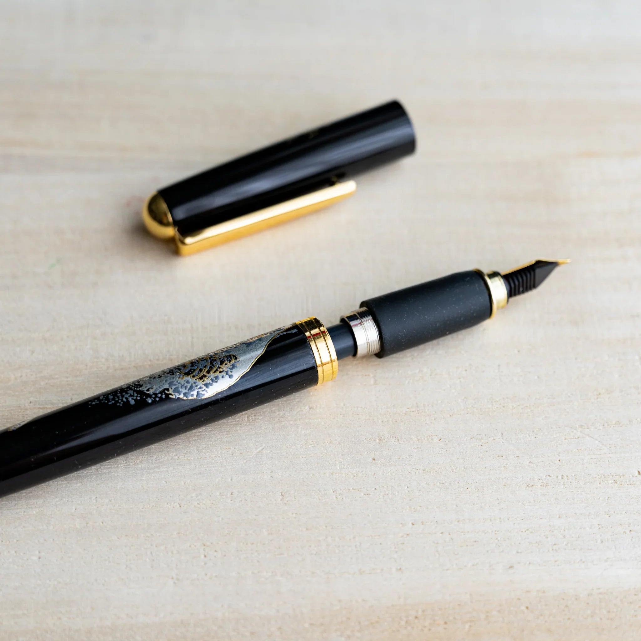 Black Yamanaka fountain pen with gold and silver urushi design, gold nib and trim, cap detached, close view on wood