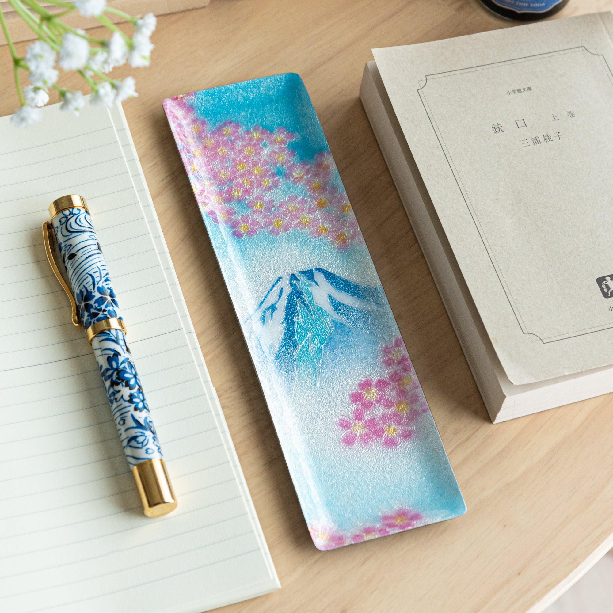 Japanese shippo ware slim pen tray with Mt. Fuji and sakura design on blue enamel, on wood desk with notebook and book
