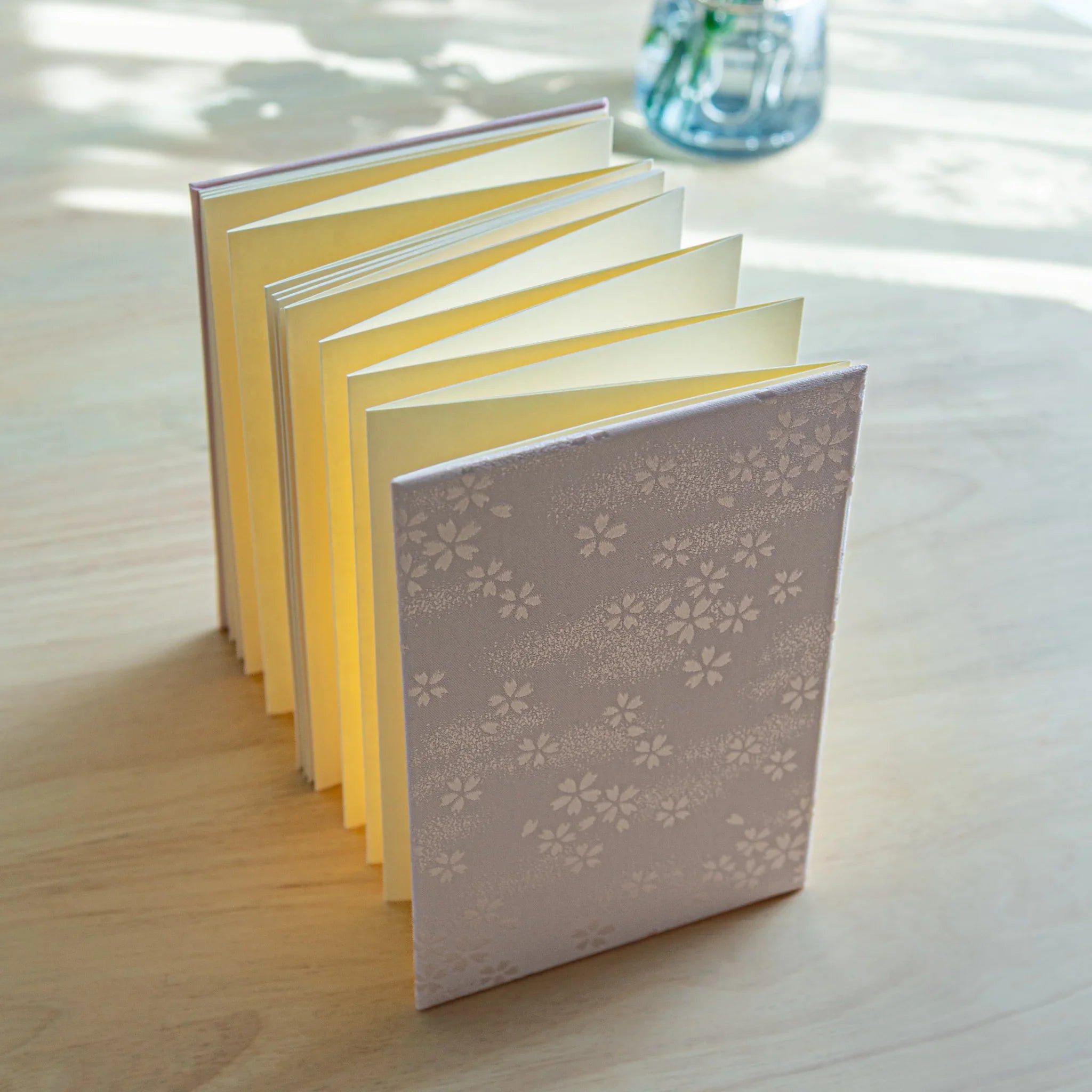 Sakura washi goshuincho stamp book standing upright with accordion fold pages fanned out showing silver sakura cover