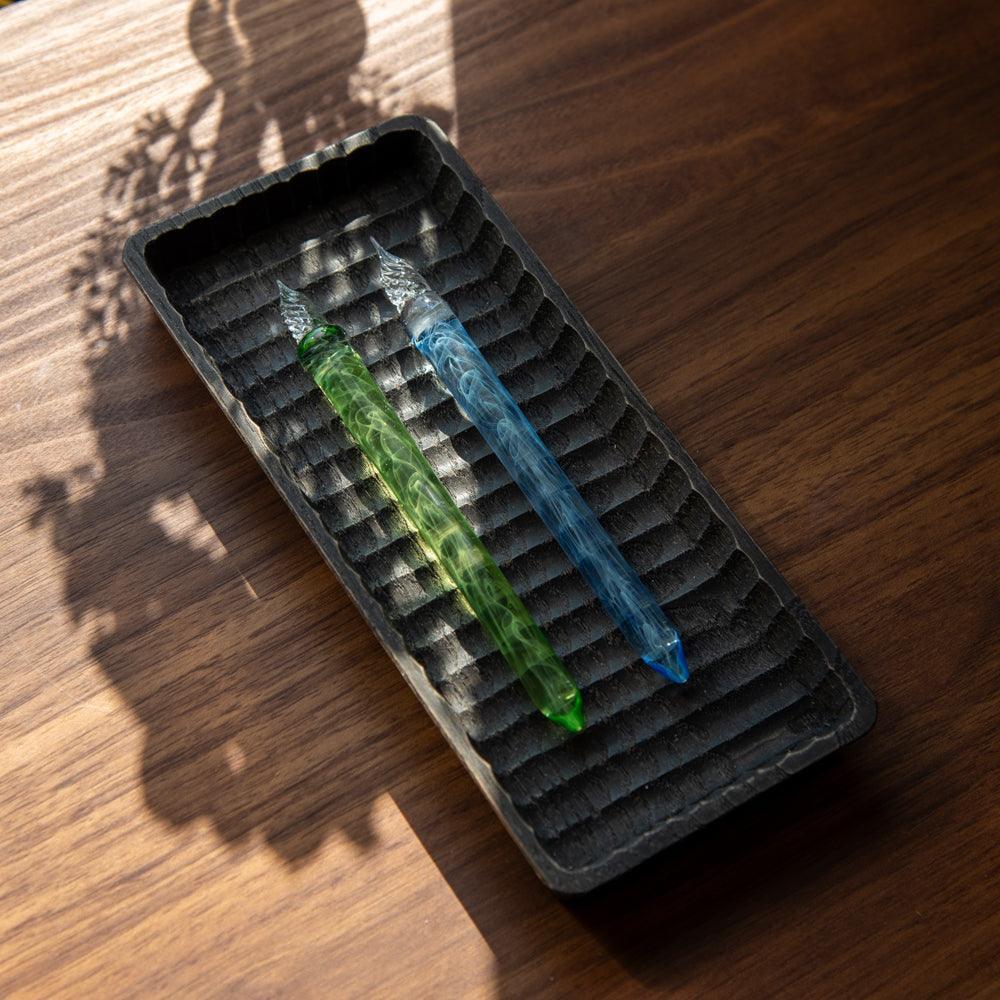 Smoke in Verdure and Azure glass dip pens arranged together in black textured tray on wooden surface