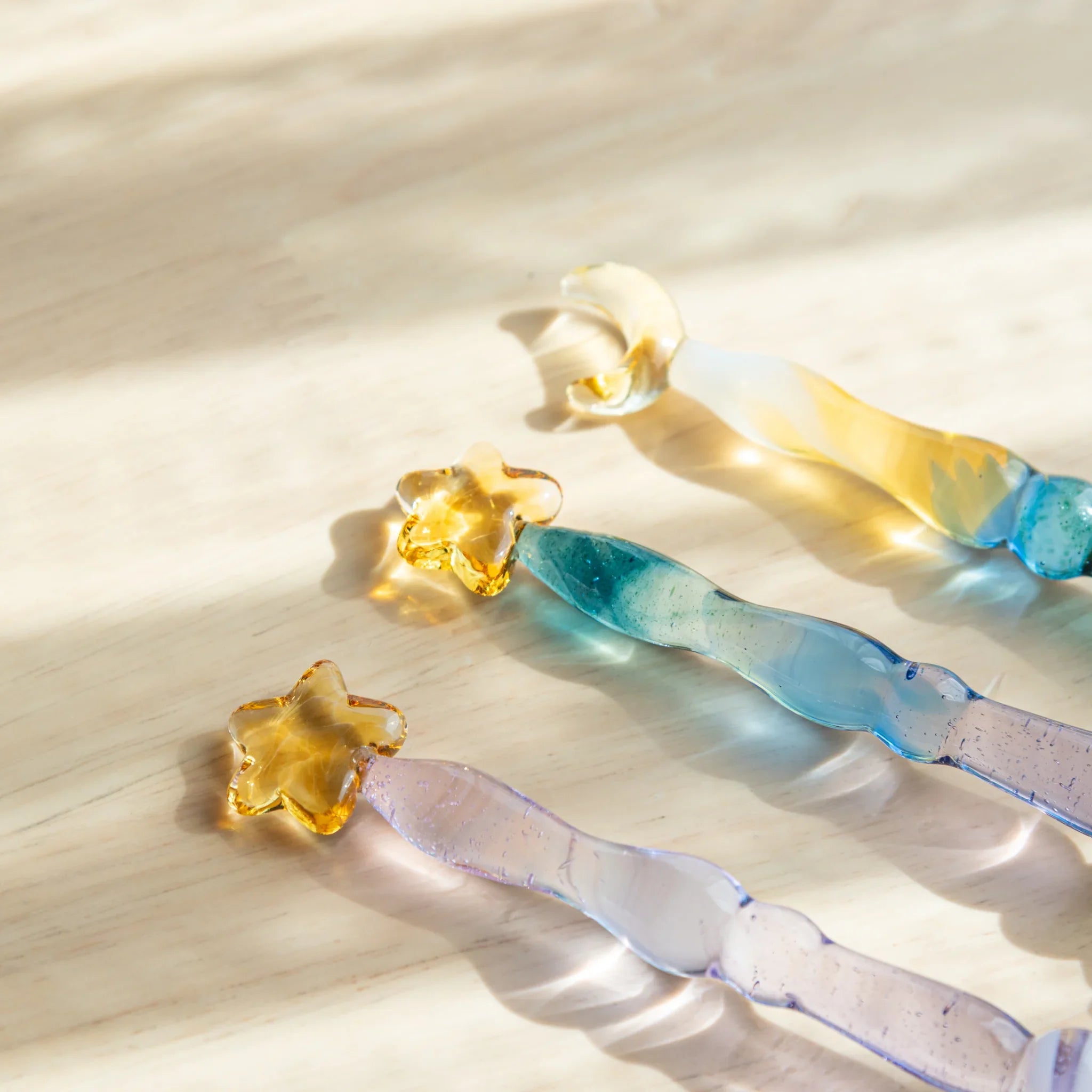 Three Starlit Night glass dip pens with star-shaped ink droplets in yellow, blue and gradient tones on wooden surface