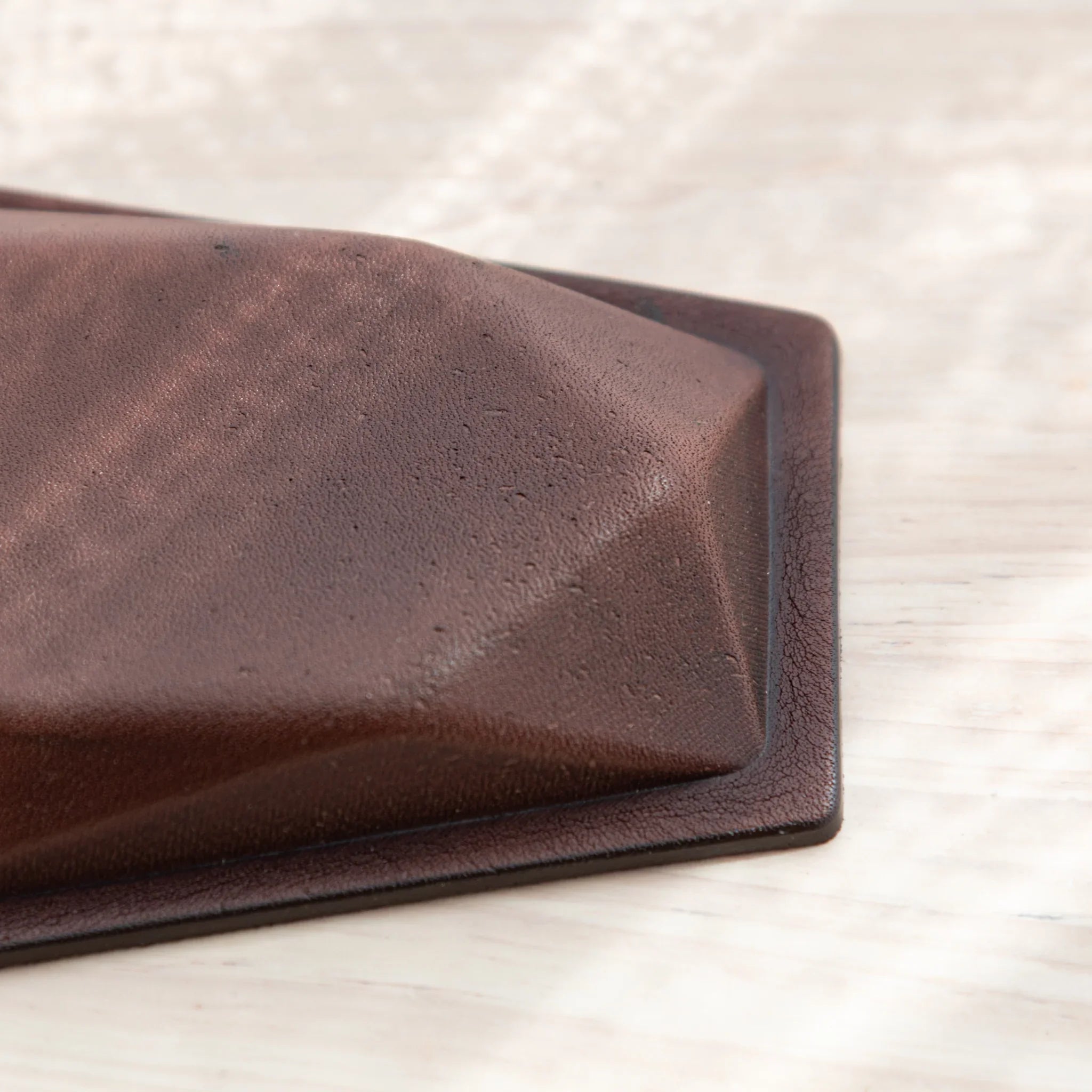 Corner detail of hexagonal pen tray showing brown leather exterior texture, angled geometric edge, and black border