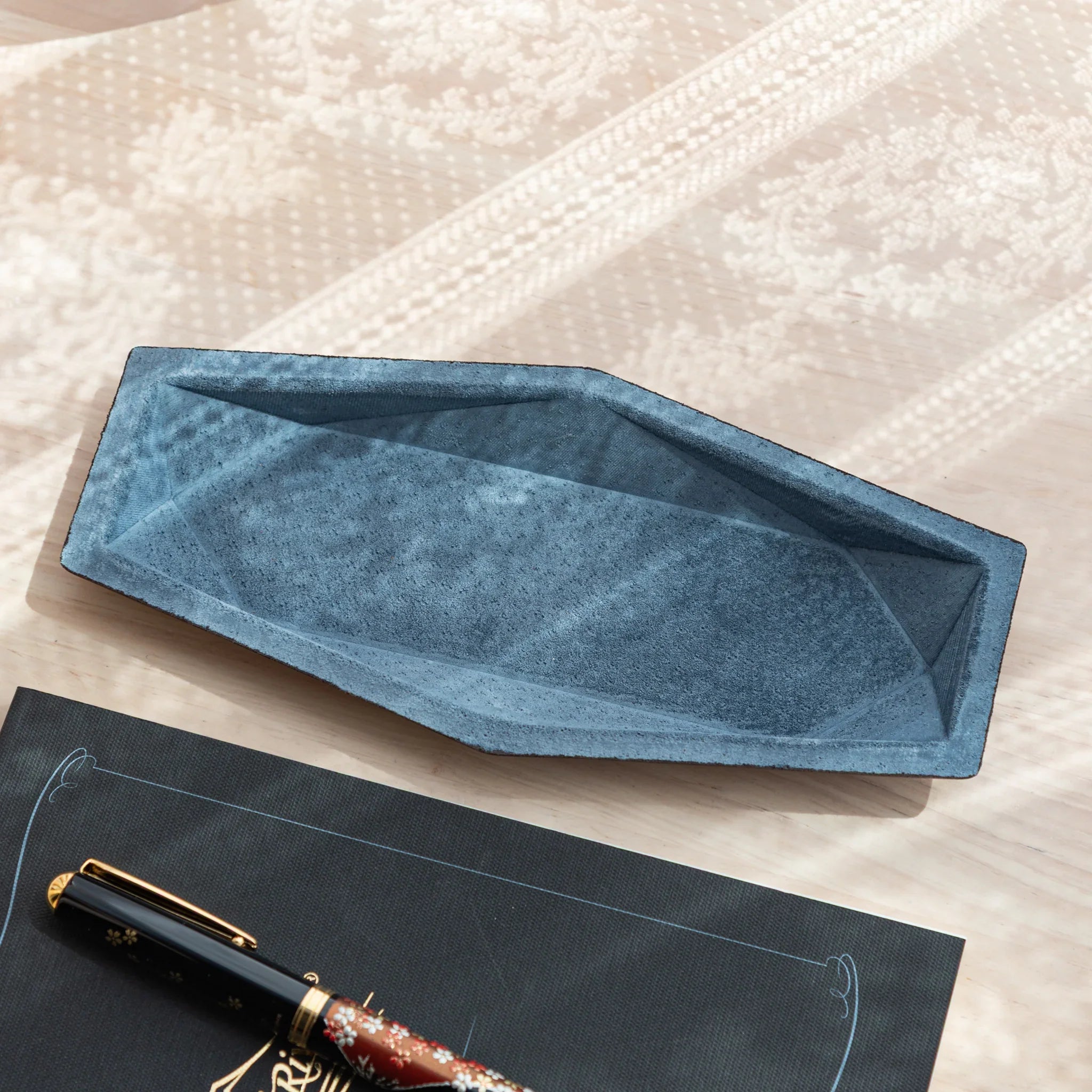 Blue-gray suede hexagonal slim pen tray shown empty from above, revealing geometric angled interior walls and suede texture