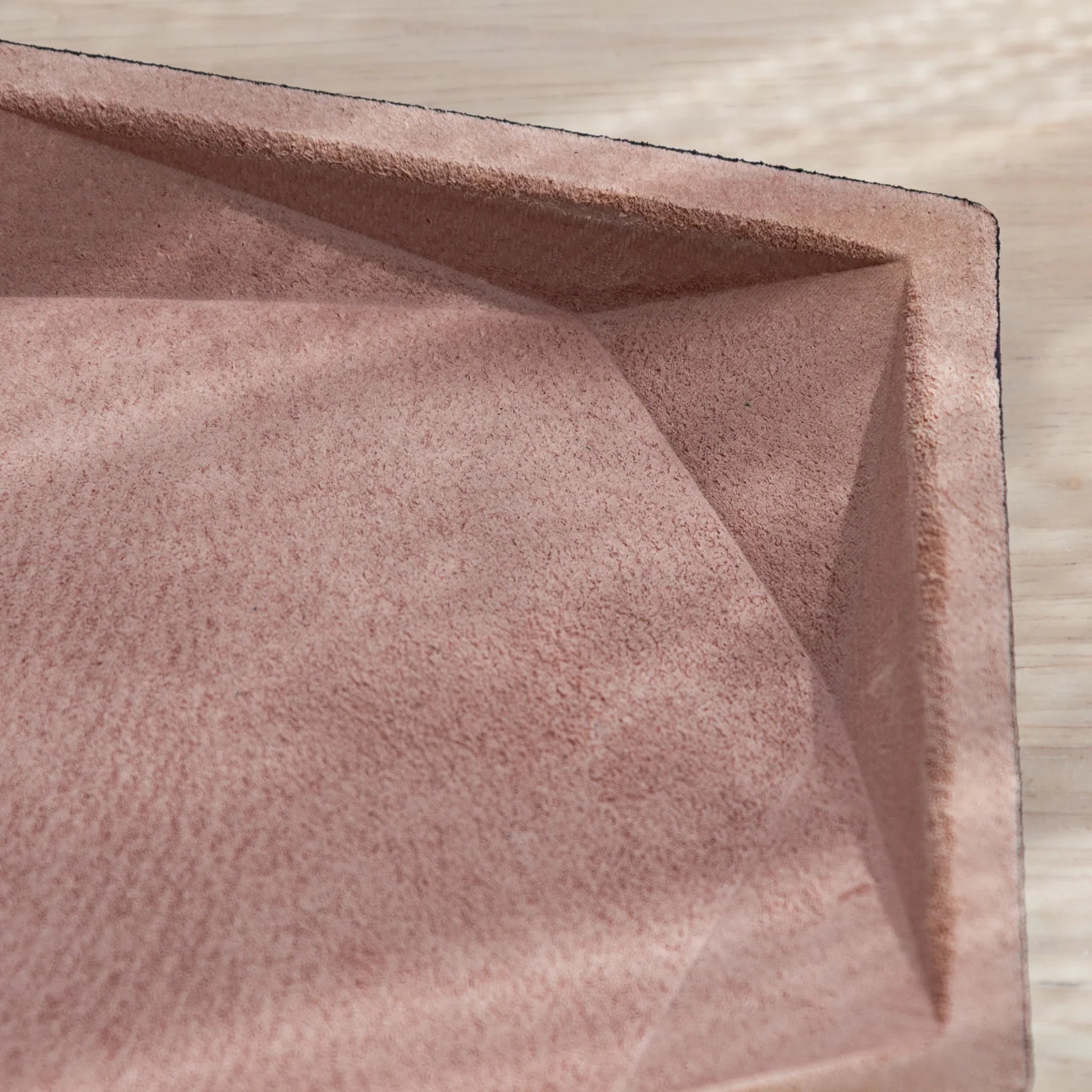 Close-up of pink suede wide hexagonal pen tray interior corner showing angled geometric wall panels and black leather rim