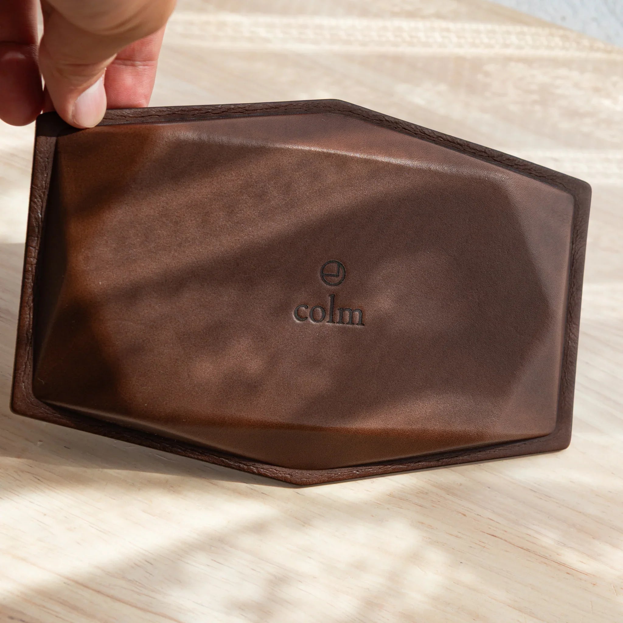 Hand tilting pink suede wide hexagonal pen tray to reveal brown leather base with embossed colm logo and hexagonal border