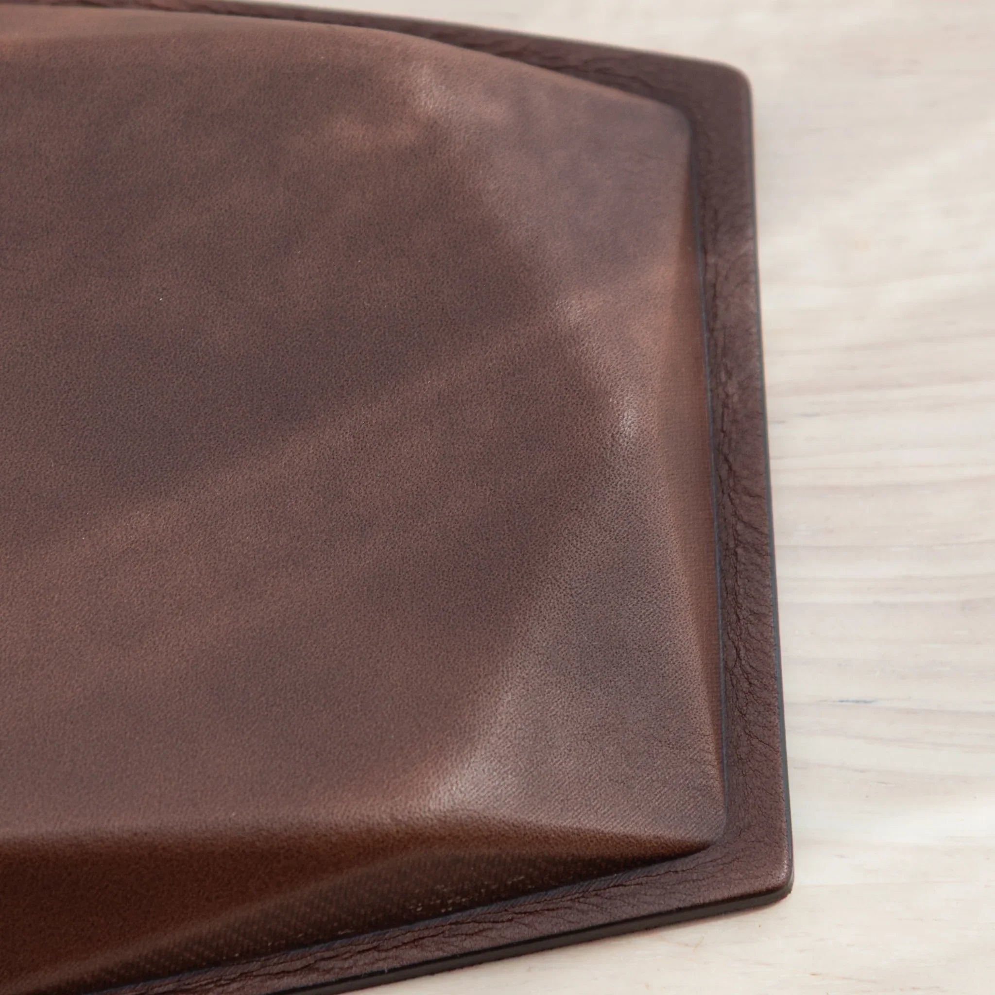 Corner detail of brown leather base of wide hexagonal pen tray showing leather grain texture and black leather border