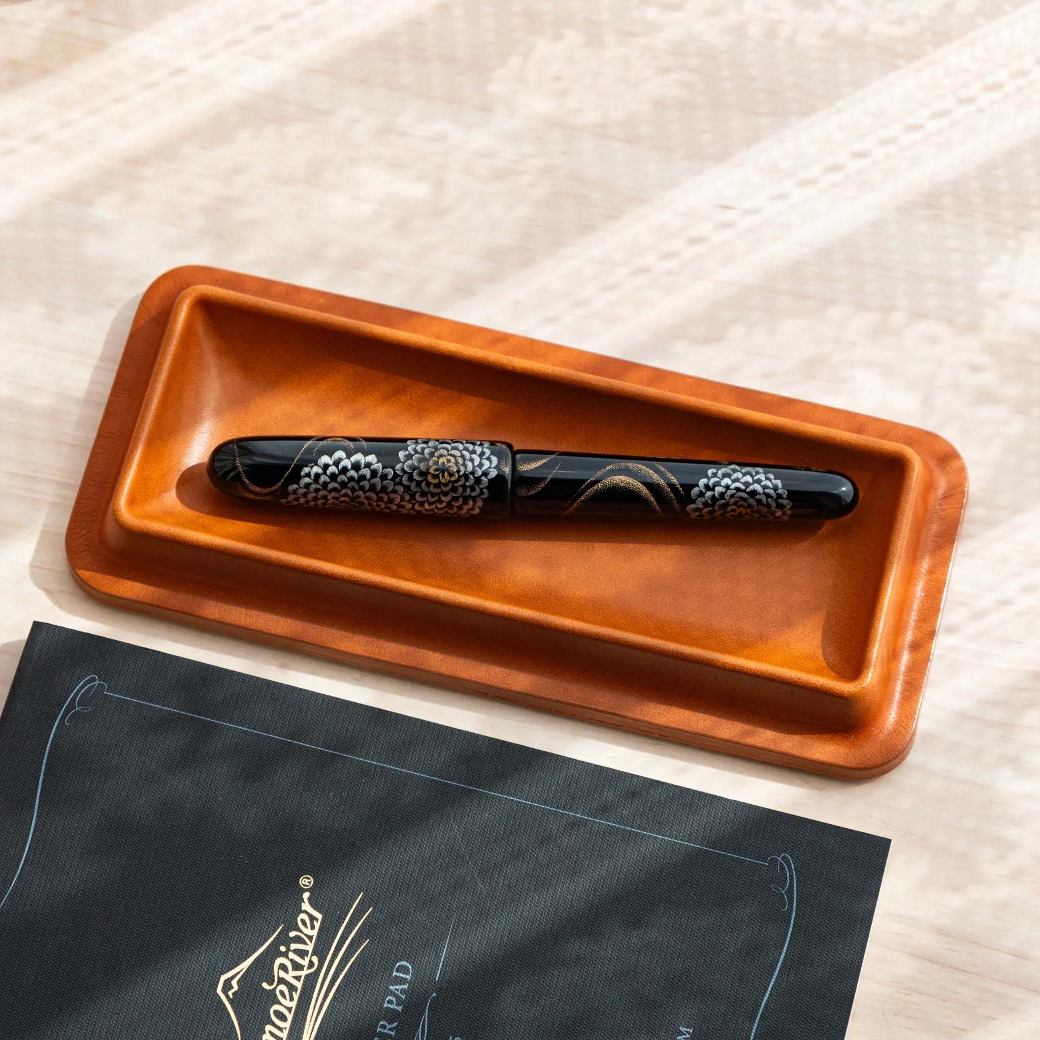 Cognac colored leather pen tray shown from overhead angle with black maki-e pen and Tomoe River paper