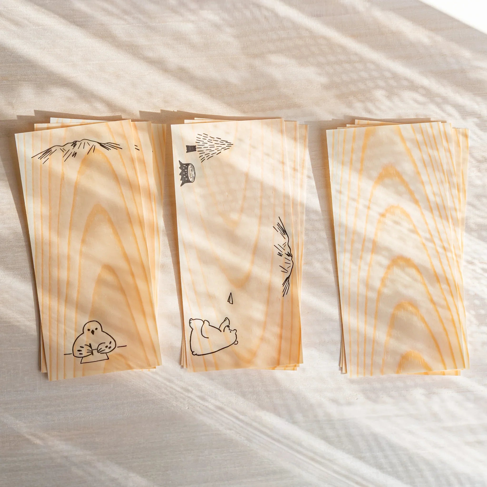 Japanese thin wood message cards arranged in three stacks on light desk showing natural pine grain with animal art