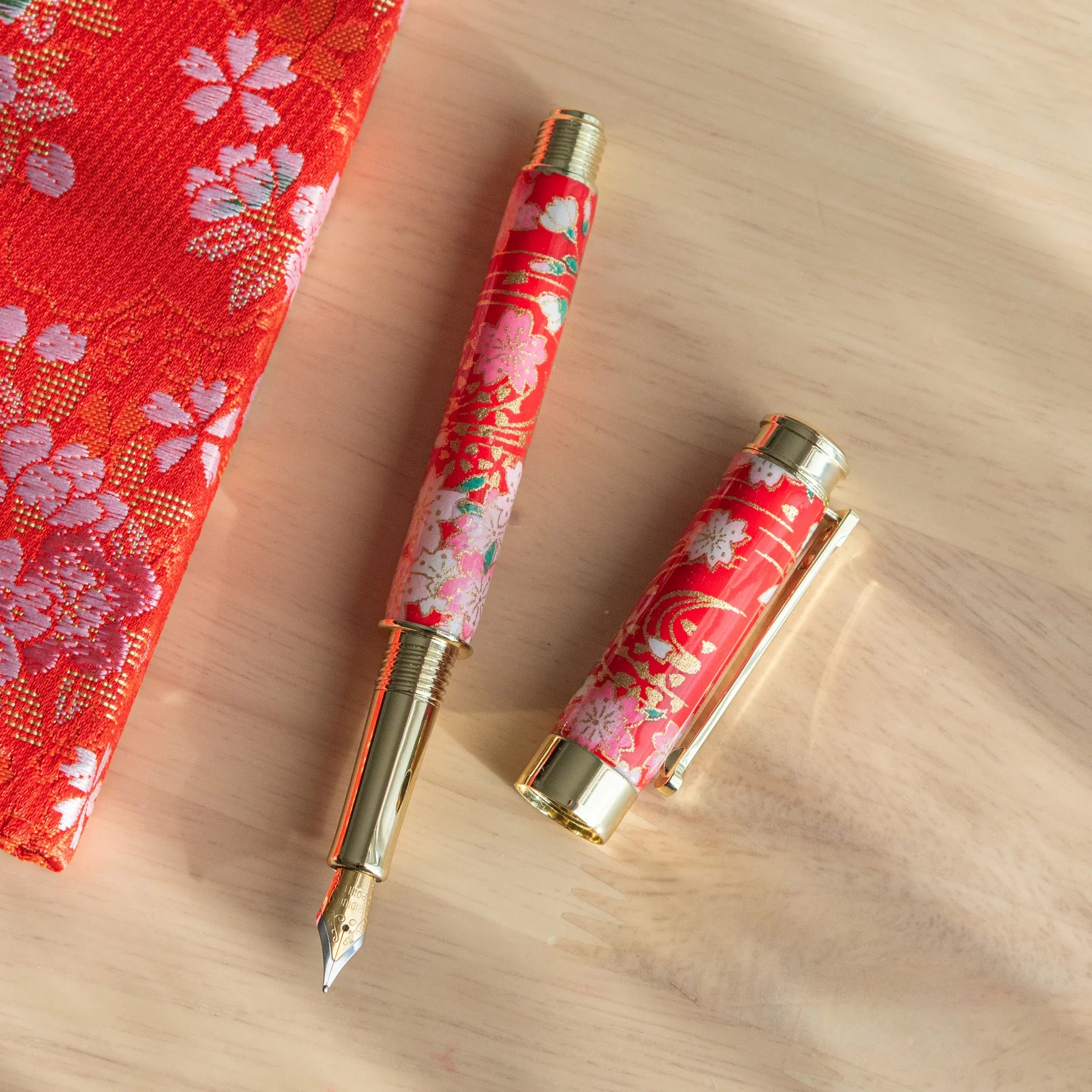 Weeping Sakura Mino washi fountain pen displayed on red botanical fabric with white cherry blossom design angle