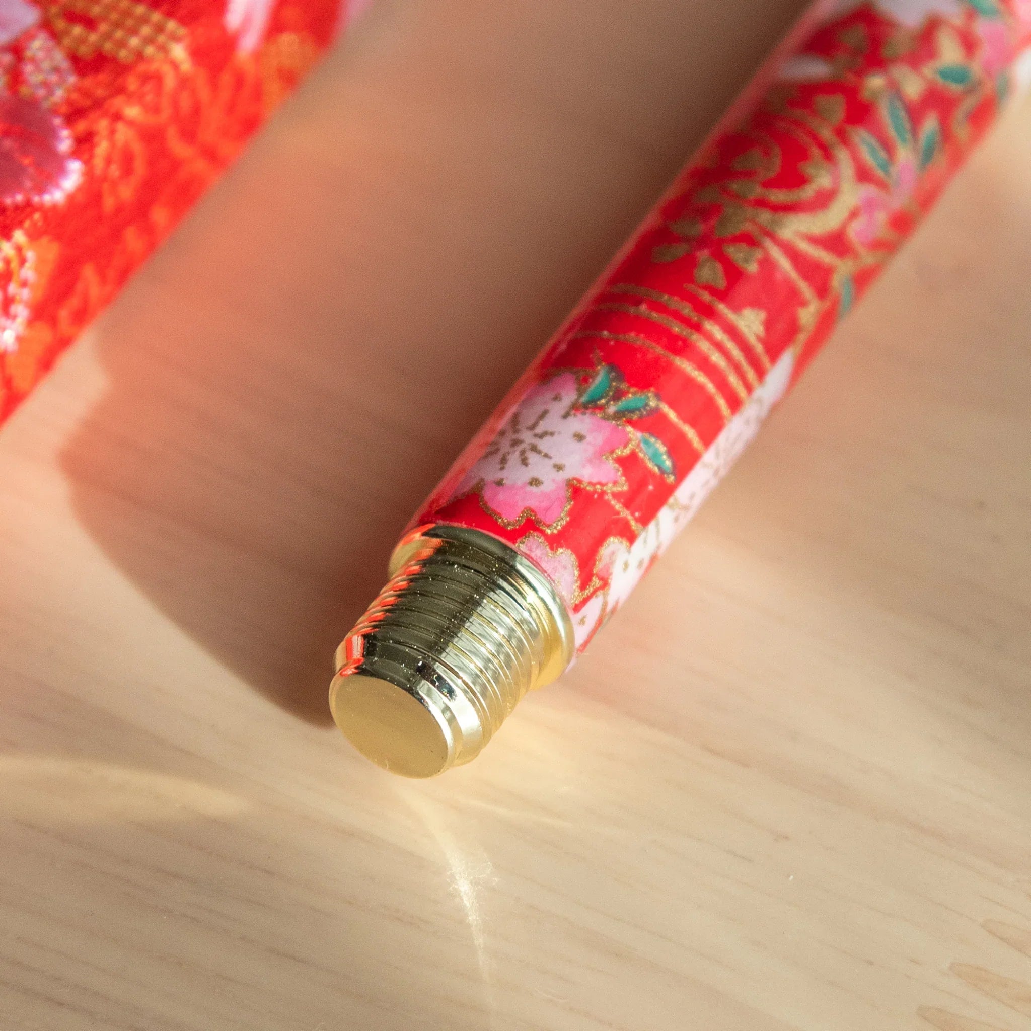 Weeping Sakura Mino Washi fountain pen cap with metallic gold trim on red botanical patterned wrapper angled view
