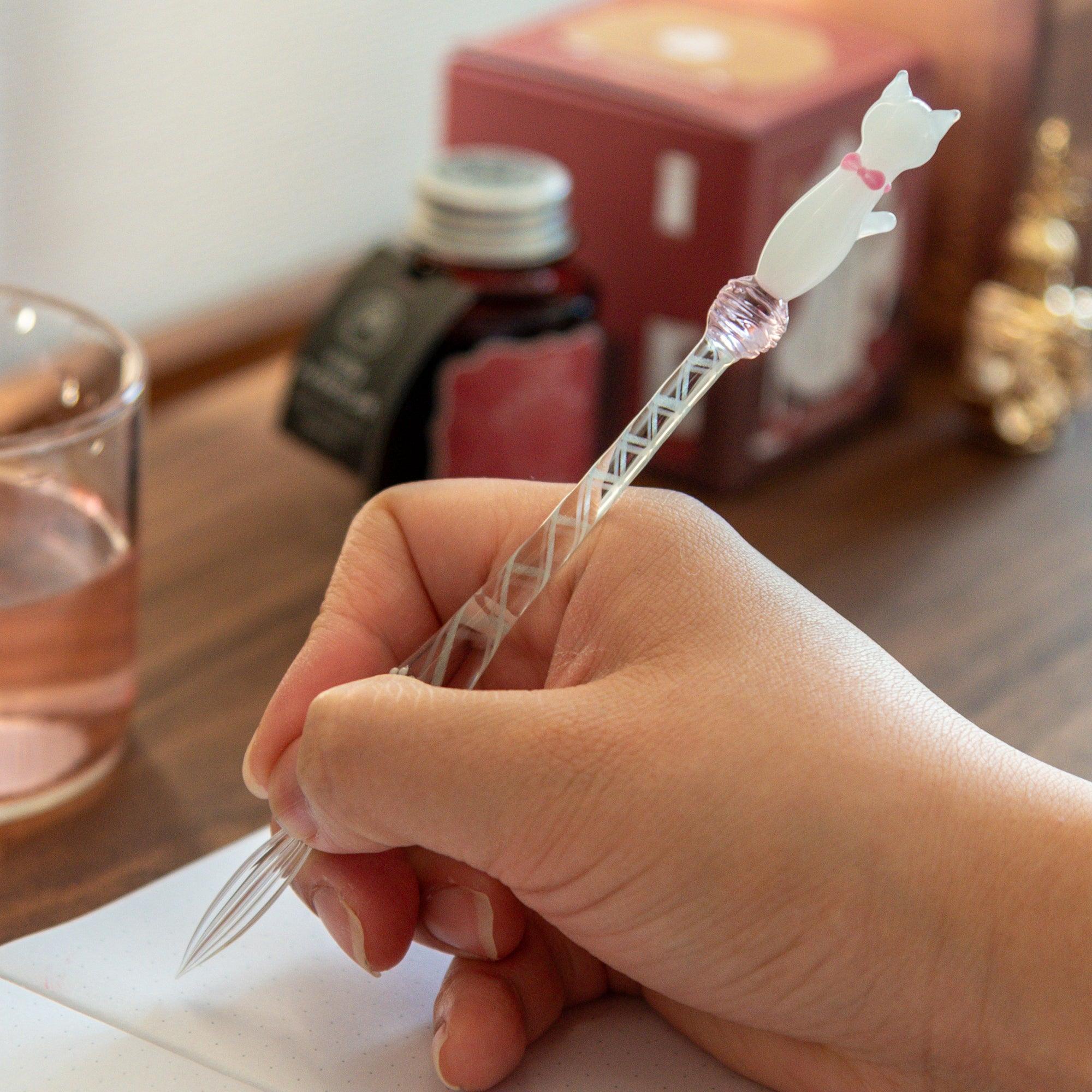 White Nyanko cat glass dip pen held in hand with clear glass barrel and pink decorative bead ornament