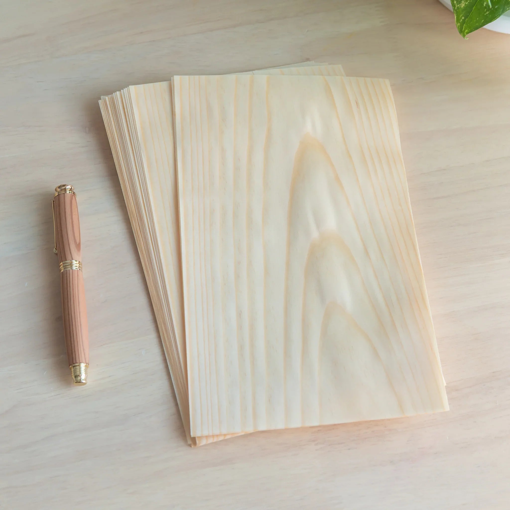 Stack of Japanese wooden loose leaf sheets showing natural pine grain, fanned slightly, with wooden barrel pen on light wood