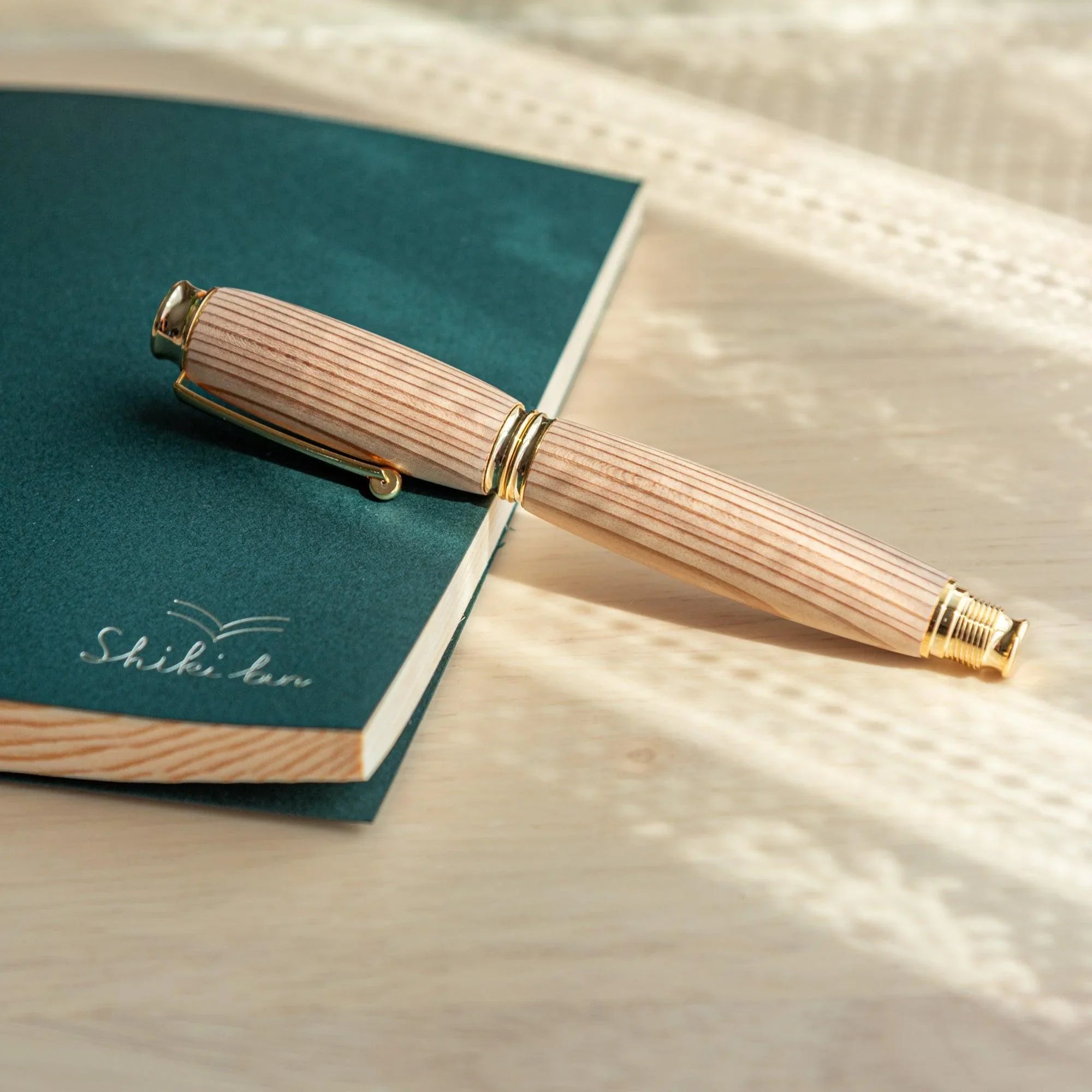 Pale cedar wood Japanese fountain pen body with prominent straight grain resting on a dark green Shiki An notebook