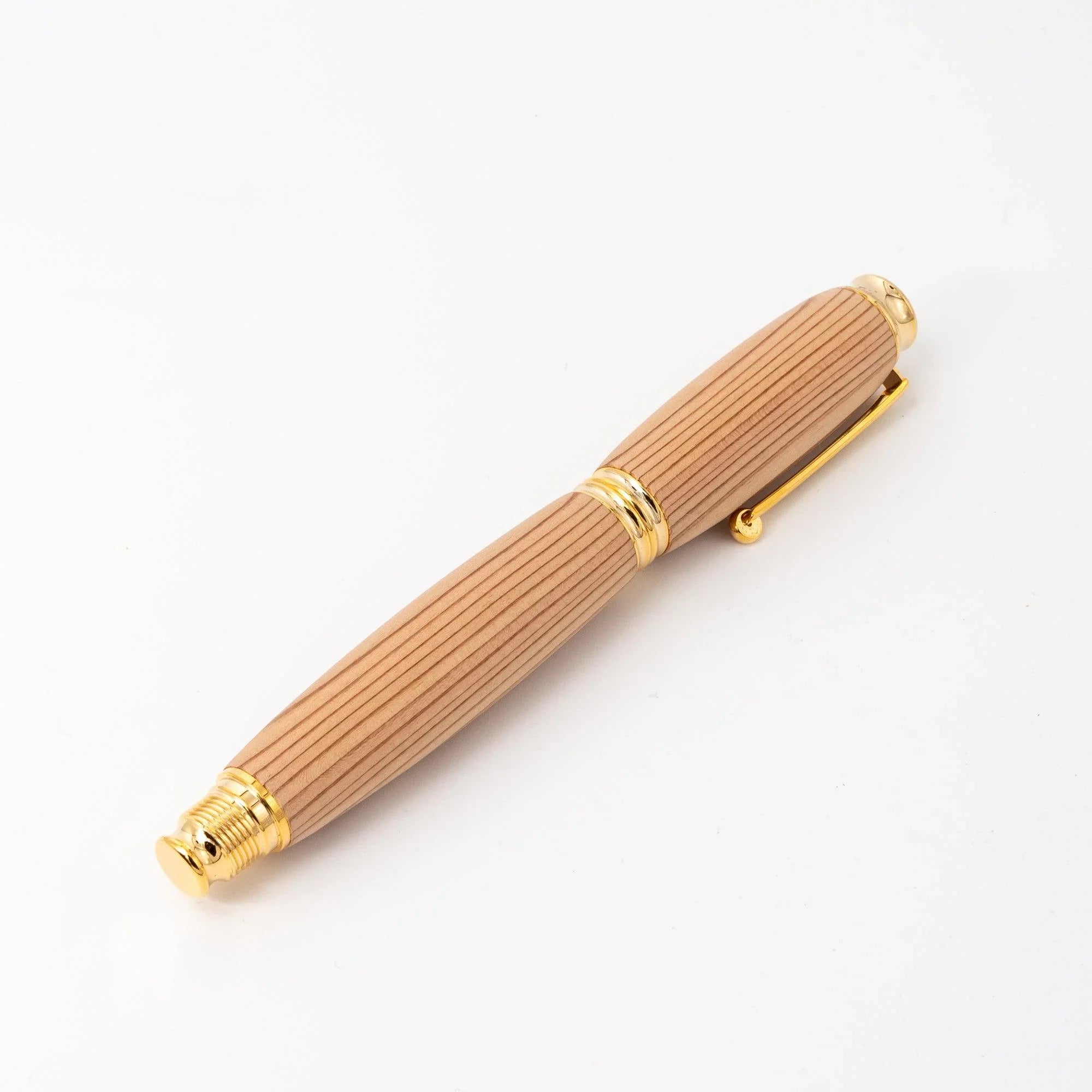 Cedar wood Japanese fountain pen capped on white background, straight wood grain, gold clip and trim rings visible