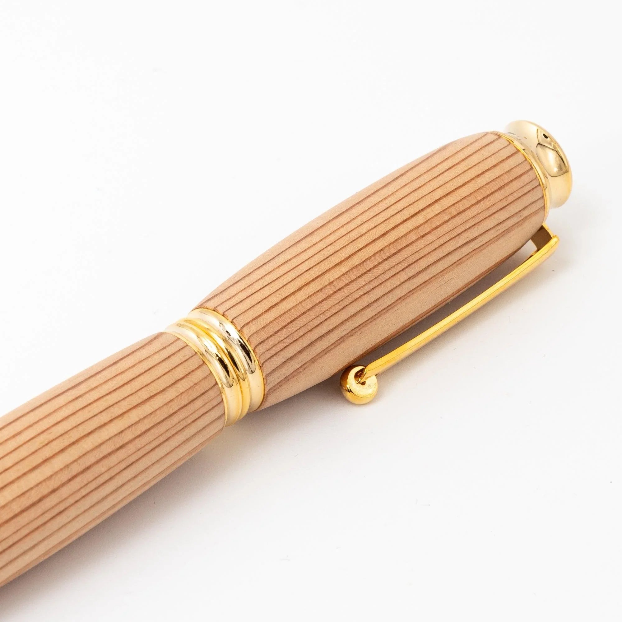 Close-up of cedar wood Japanese fountain pen cap showing straight grain, gold trim rings, and gold clip on white background