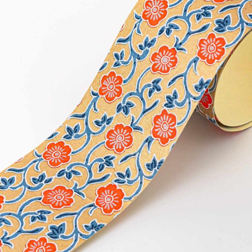 Close-up of Red Flower yuzen washi tape showing coral-red plum blossoms on blue arabesque vine lattice over gold ground